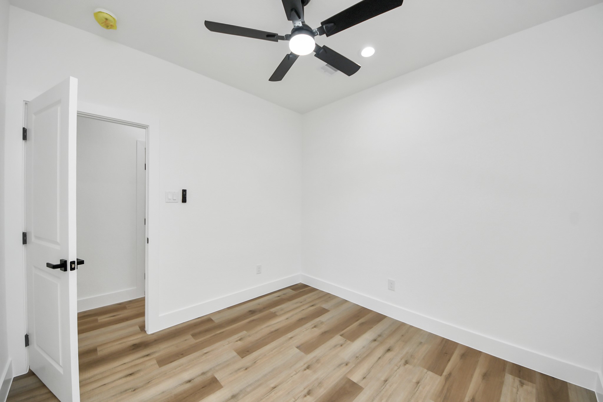 Bright and inviting room featuring sleek hardwood flooring, modern recessed lighting, and a stylish ceiling fan for added comfort.
