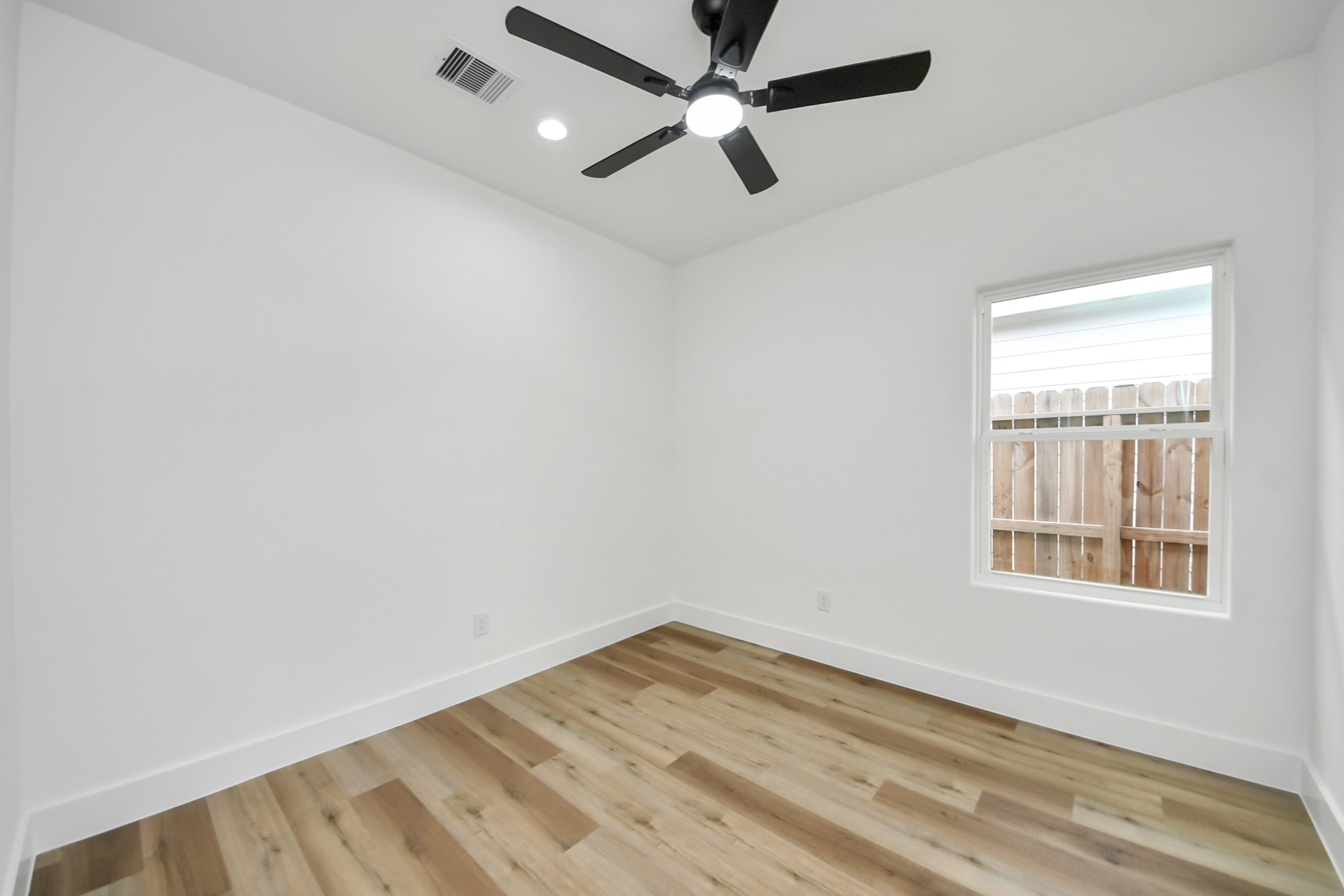 Bright room with sleek wood flooring, modern ceiling fan, and ample natural light from the window.
