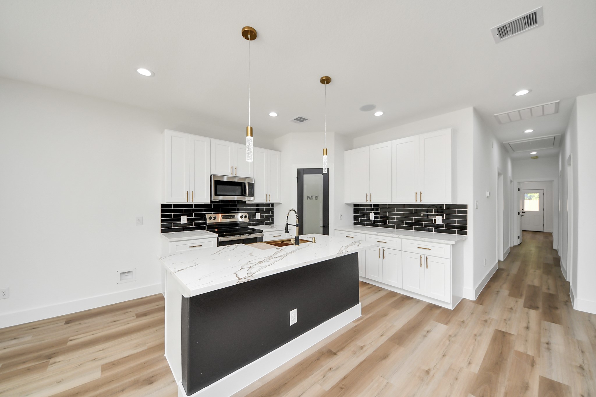 Sleek modern kitchen featuring a spacious island with a marble countertop, elegant black backsplash, and stainless steel appliances, complemented by warm wood flooring.