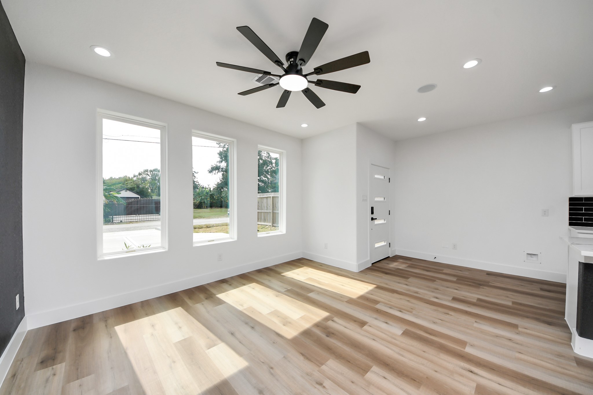 Bright and airy living space featuring large windows, sleek ceiling fan, and elegant wood flooring, offering a welcoming and modern ambiance.