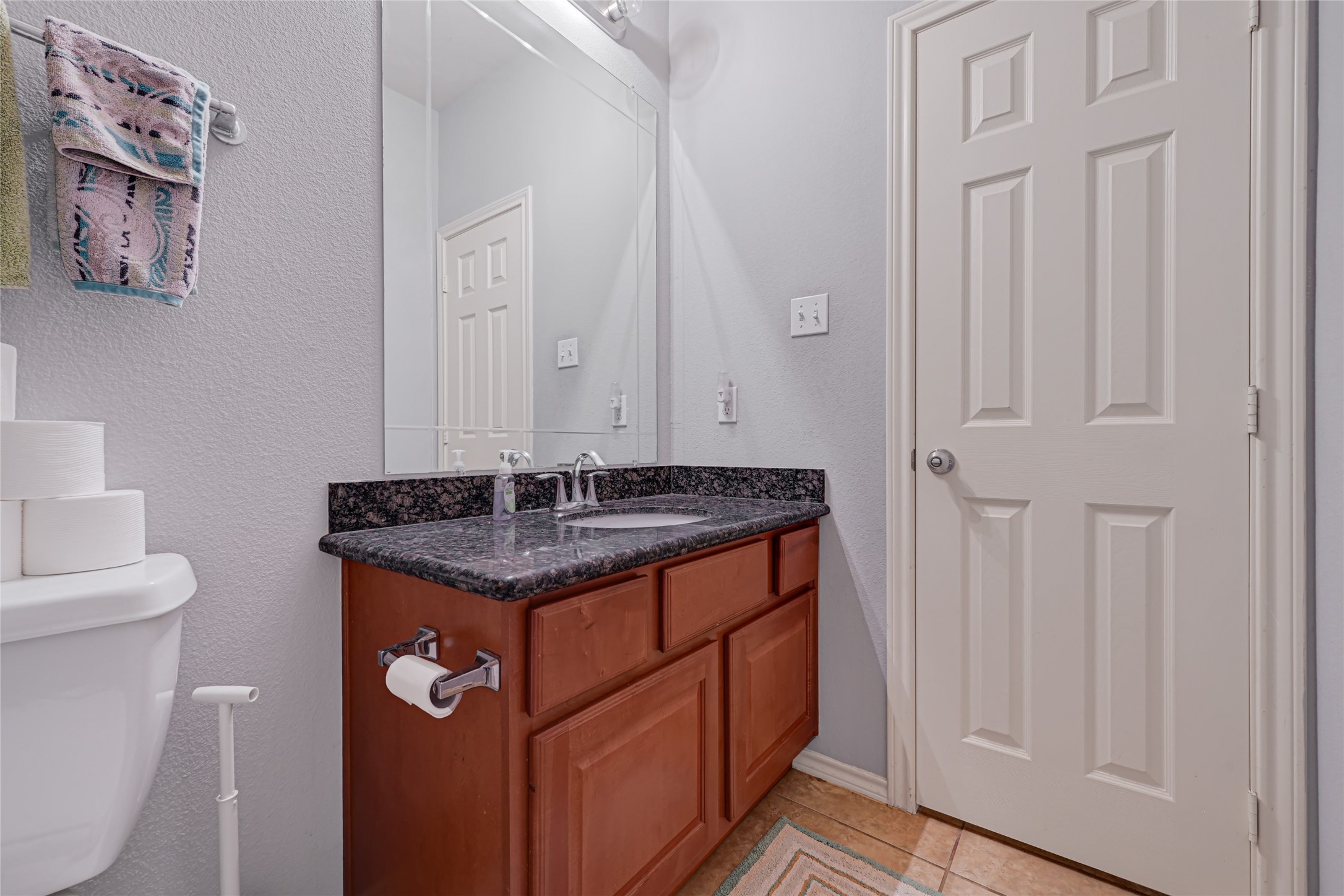 Charming bathroom featuring a sleek granite countertop, ample cabinet storage, and a large mirror, complemented by neutral tile flooring for a clean, modern look.