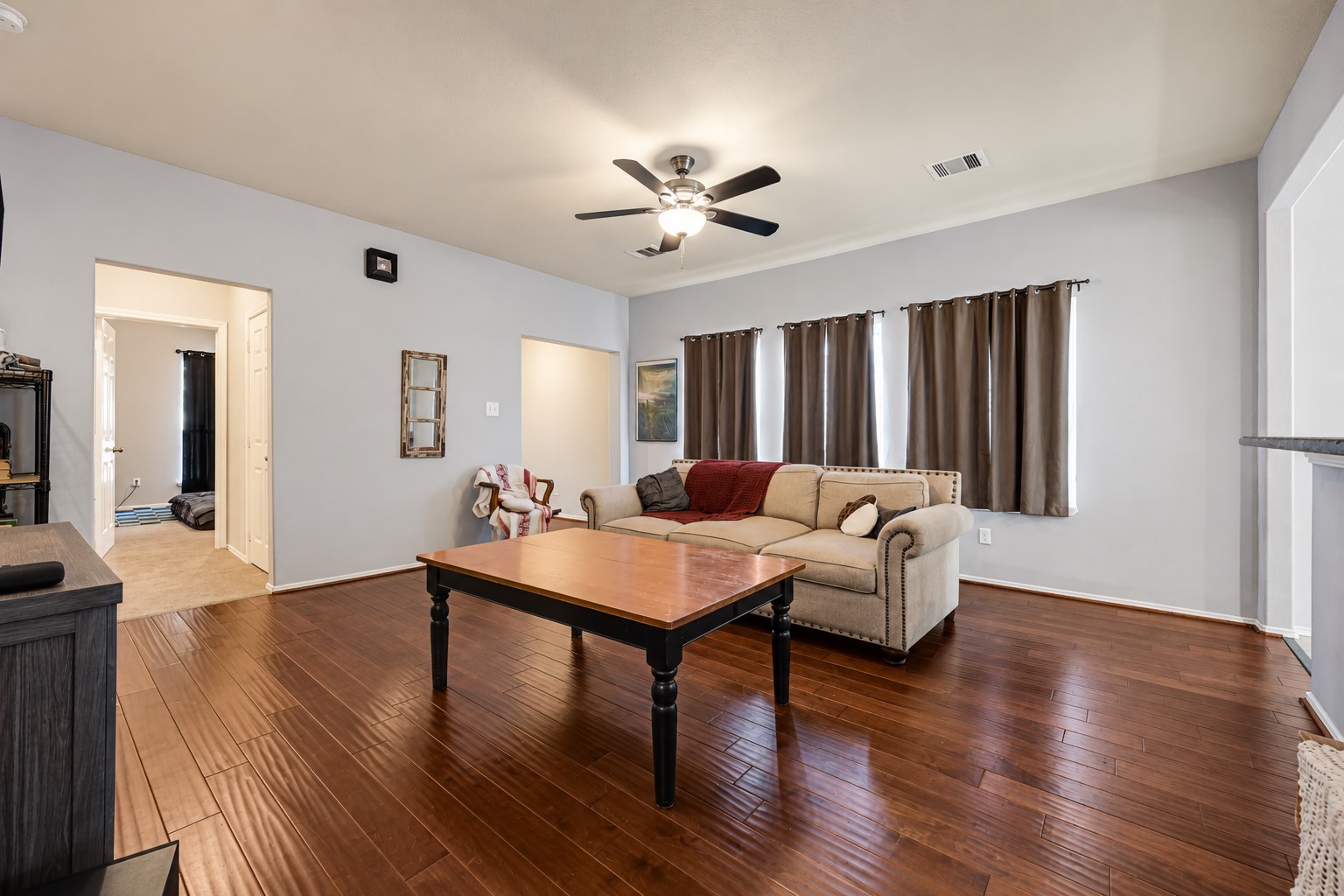 Spacious living room with rich hardwood floors, a cozy sofa, and ample natural light from large windows, perfect for relaxation and entertaining.