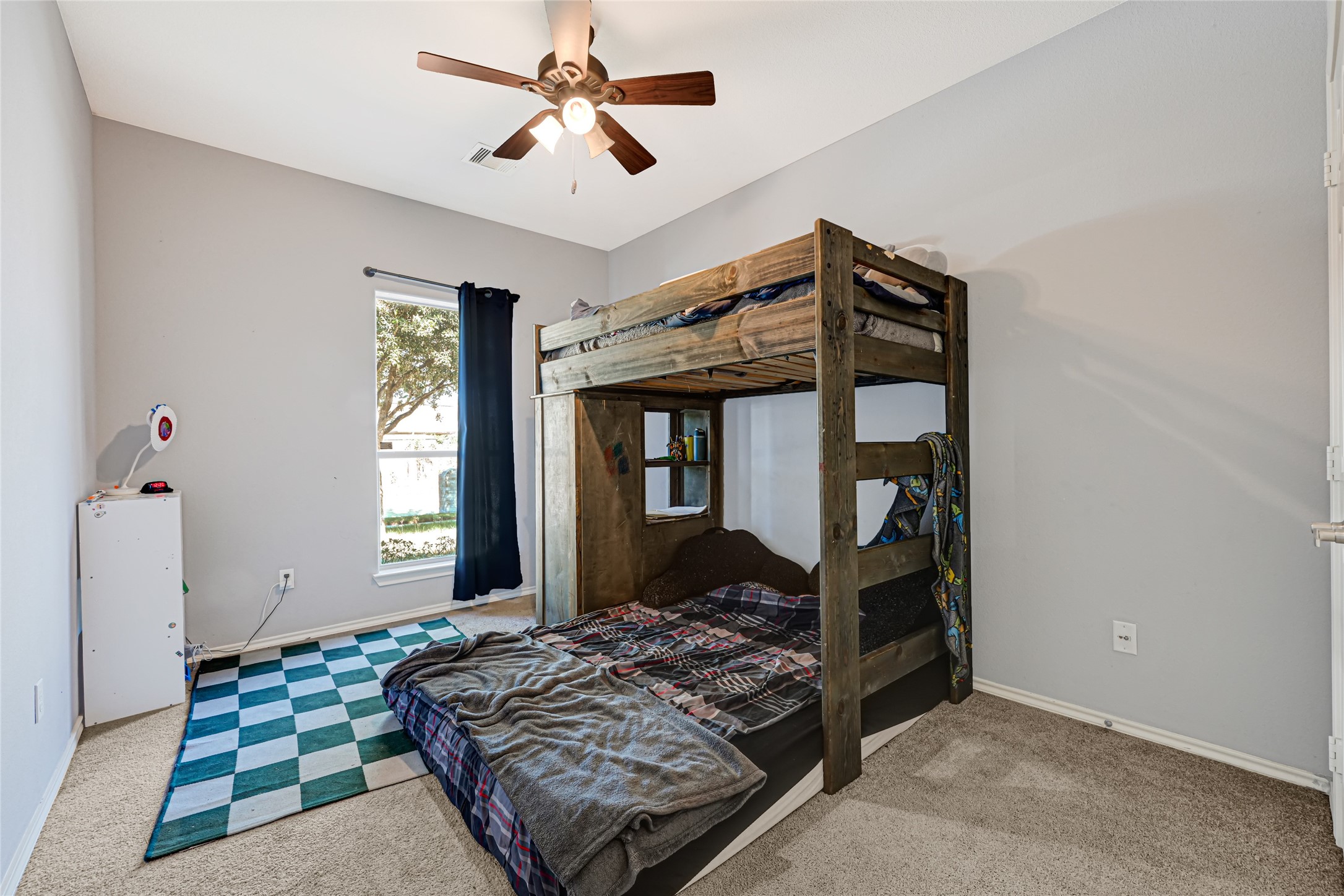 Cozy bedroom with a wooden bunk bed, soft carpeting, and ample natural light from a large window, creating a welcoming atmosphere.