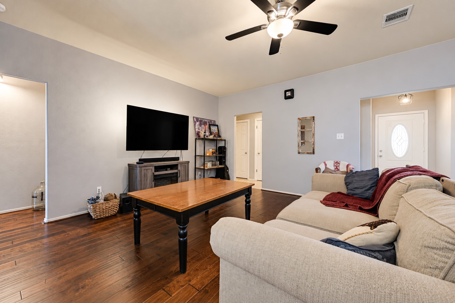 Spacious living room with warm wood flooring, a cozy sectional sofa, and a sleek ceiling fan, offering a welcoming space for relaxation and entertainment.