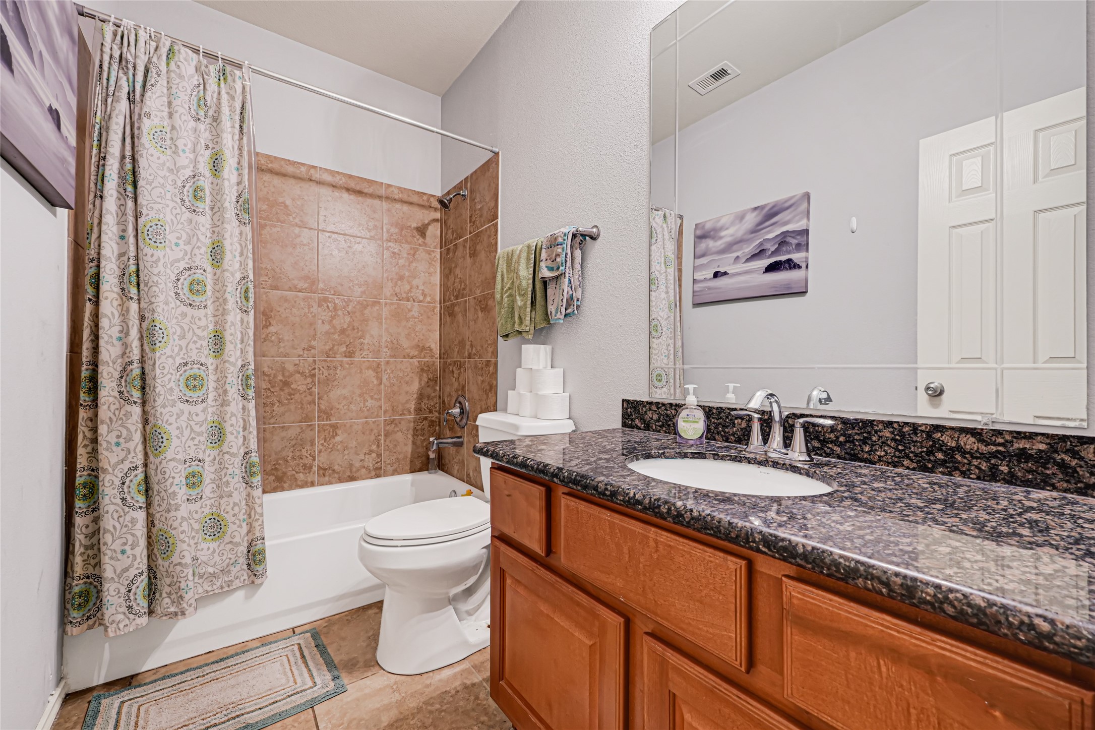 Charming bathroom featuring a granite countertop, wooden cabinetry, and a stylishly tiled shower-tub combo.