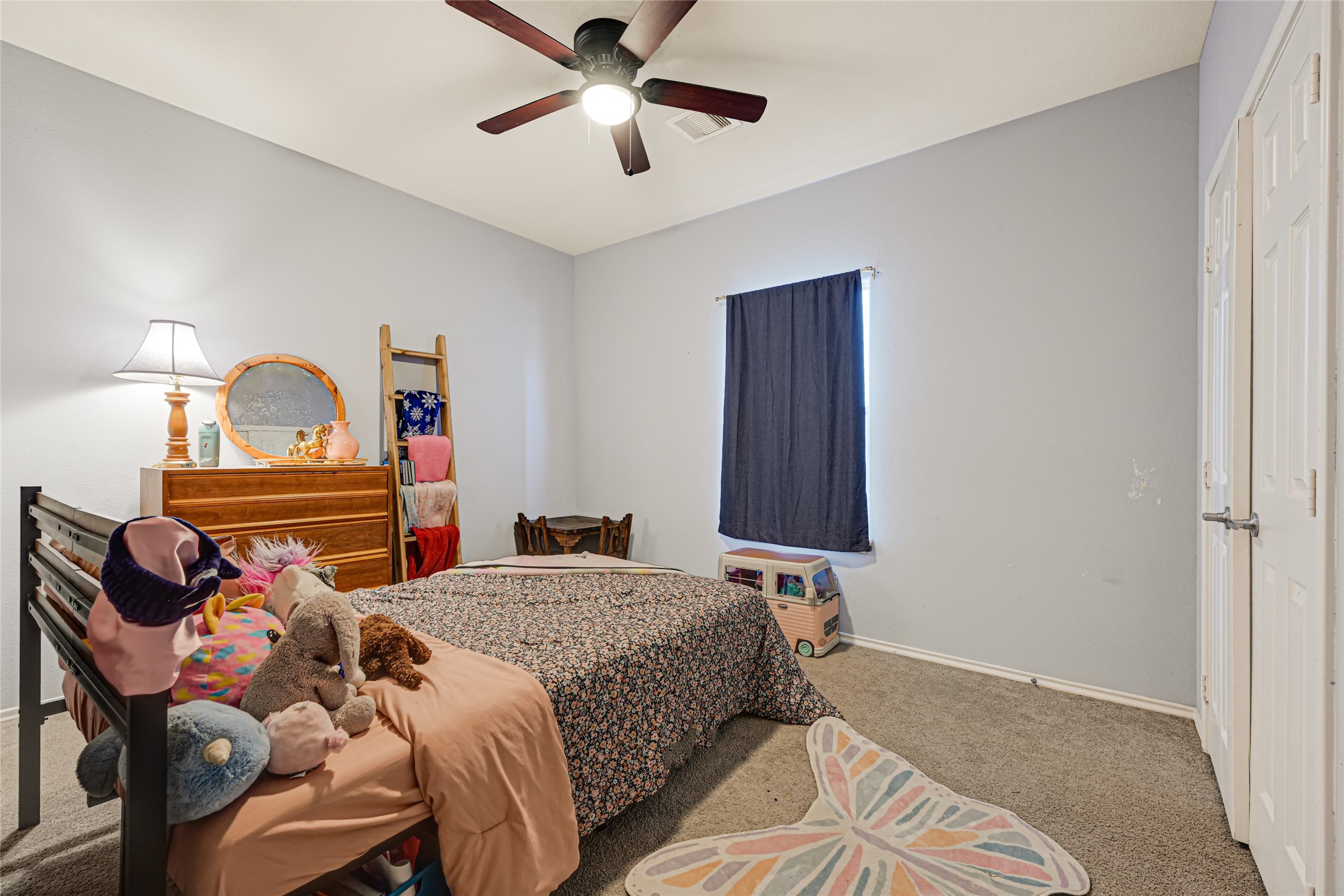 Cozy bedroom featuring soft carpet, a ceiling fan, and ample natural light, perfect for relaxation and comfort.