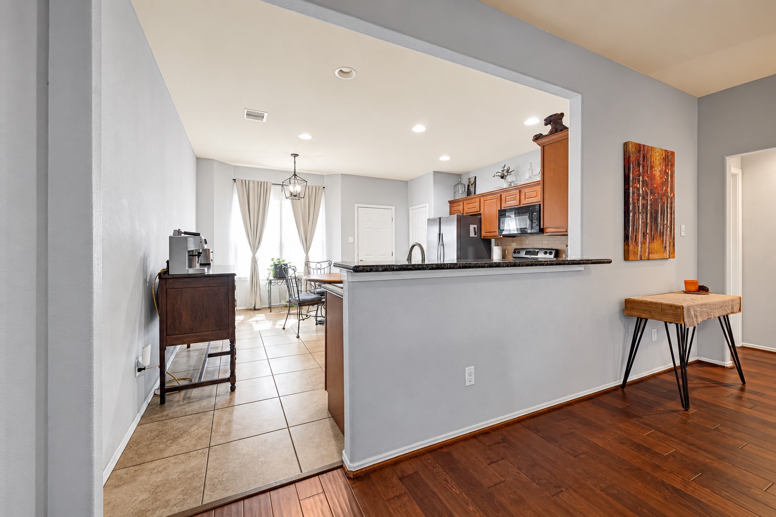 Open-concept kitchen with a breakfast bar, stainless steel appliances, and warm wood cabinetry, seamlessly flowing into a bright dining area with large windows.