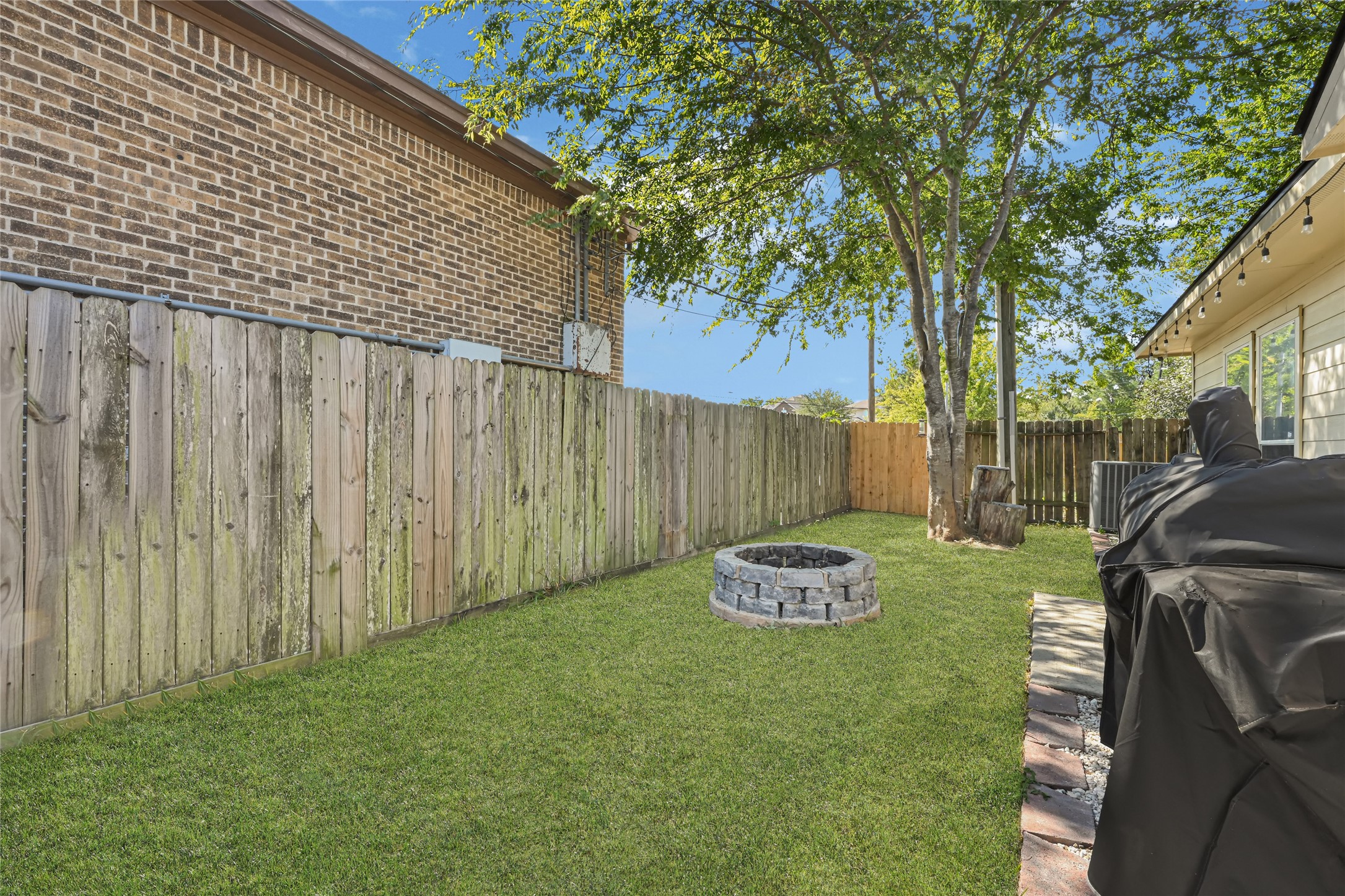 Charming backyard with lush green grass, a cozy fire pit, and ample space for outdoor gatherings, all set against a backdrop of mature trees and a privacy fence.