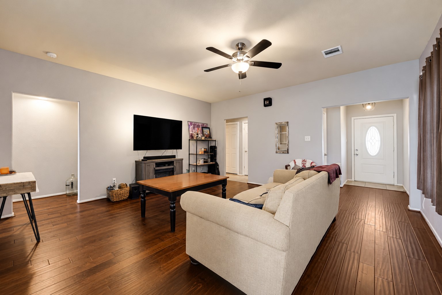 Spacious living room with warm hardwood floors, a cozy fireplace, and ample seating. The modern ceiling fan and large TV create a perfect space for relaxation and entertainment. Spacious living room with warm hardwood floors, a cozy fireplace, and ample seating. The modern ceiling fan and large TV create a perfect space for relaxation and entertainment.
