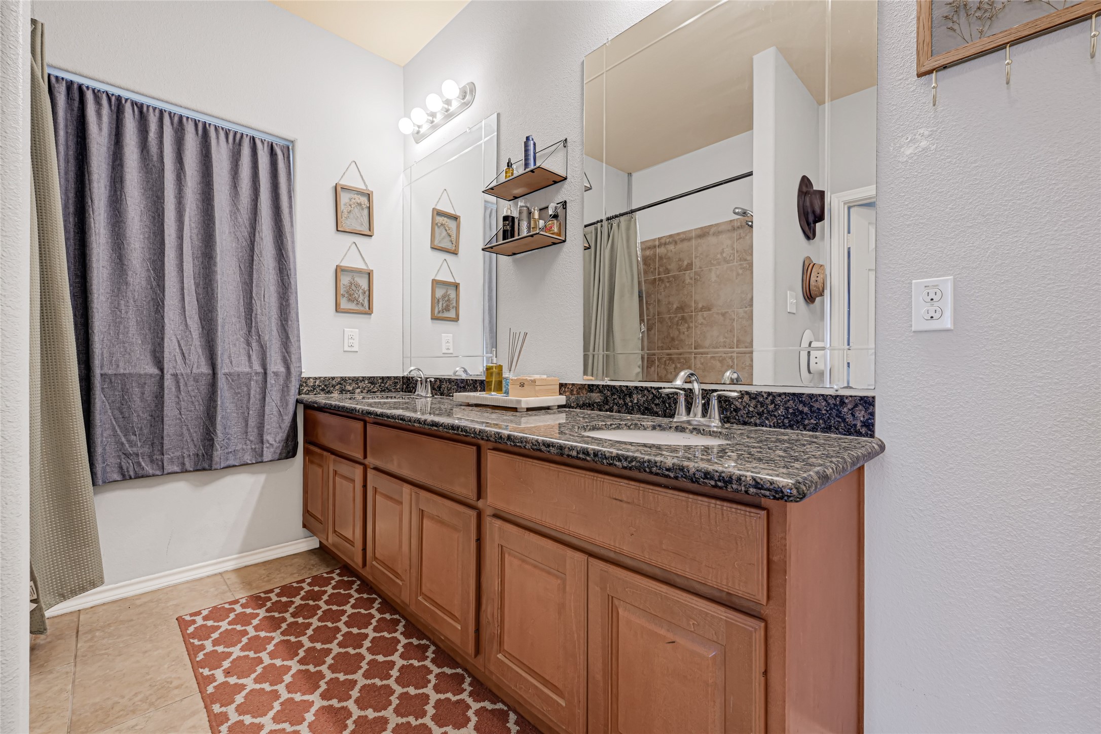 Spacious bathroom featuring a double vanity with granite countertops and ample storage, complemented by stylish lighting and a large mirror for a modern touch.