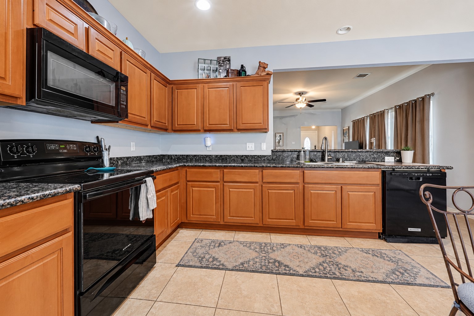 Spacious kitchen with warm wood cabinetry, sleek black appliances, and elegant granite countertops, perfect for culinary enthusiasts.