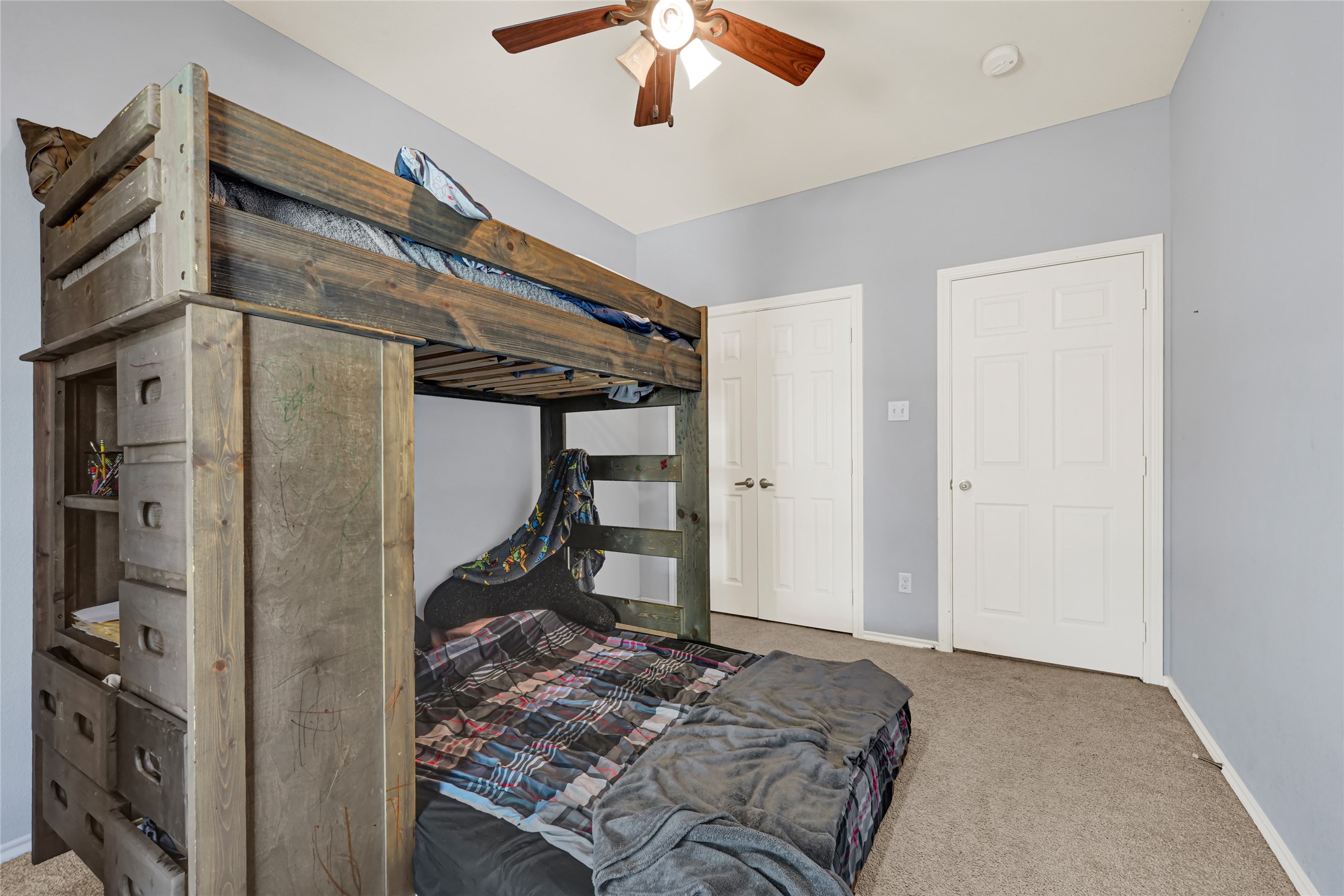 Cozy bedroom with a rustic wooden bunk bed, soft carpeting, and a ceiling fan, perfect for a child's retreat.