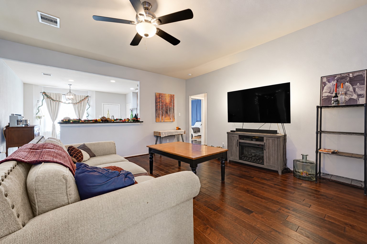 Spacious living room with warm wooden floors, a cozy sectional sofa, and a large flat-screen TV, perfect for relaxation and entertainment.