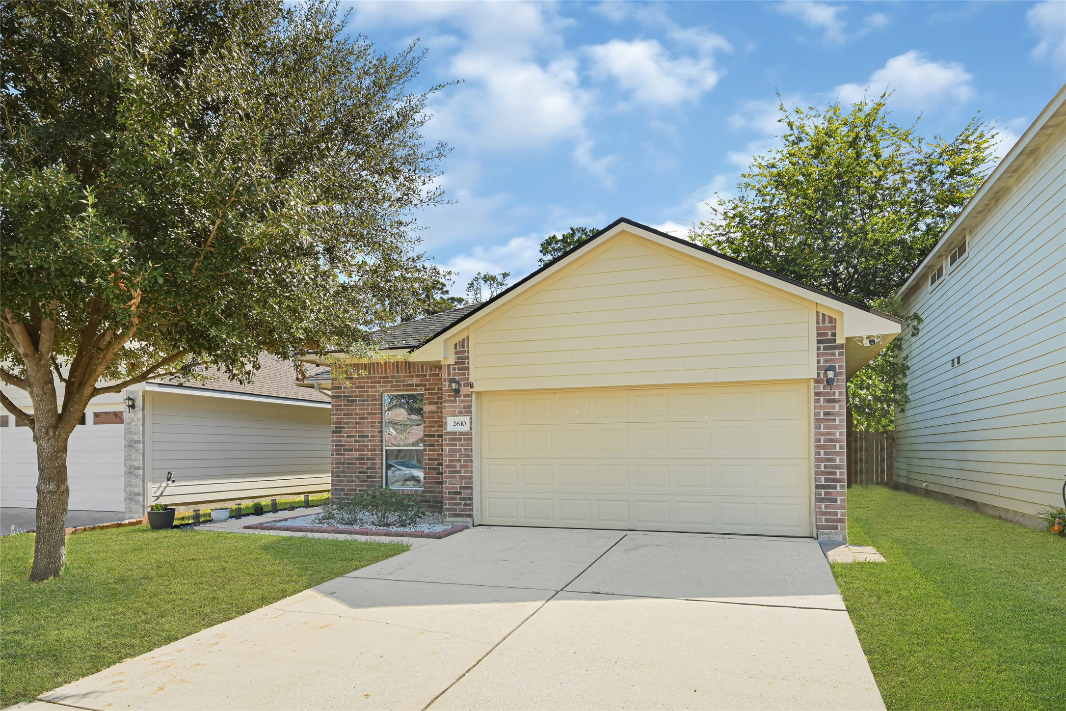 Charming single-story home with a two-car garage, brick accents, and a well-maintained front yard featuring a mature tree.