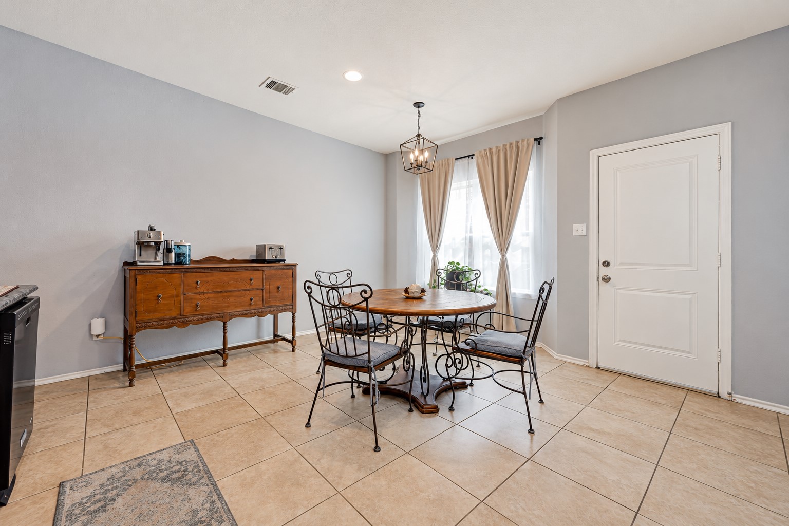 Dining area featuring the elegant chairs complimenting the wood furniture atop a tiled floor. A small light fixture atop gives a warm and inviting sense of lighting.