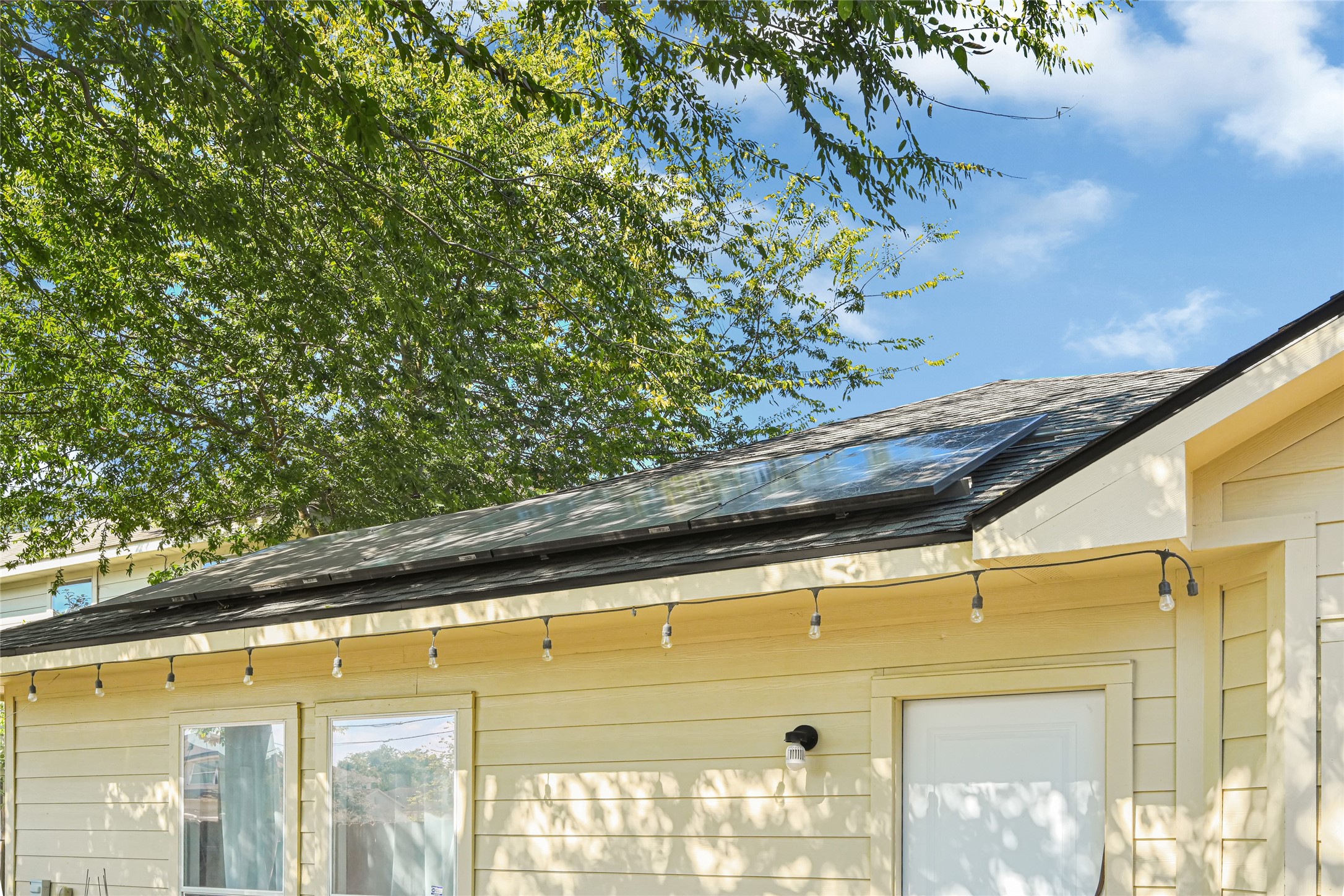 Charming home with energy-efficient solar panels and inviting outdoor lighting, nestled under the shade of mature trees.