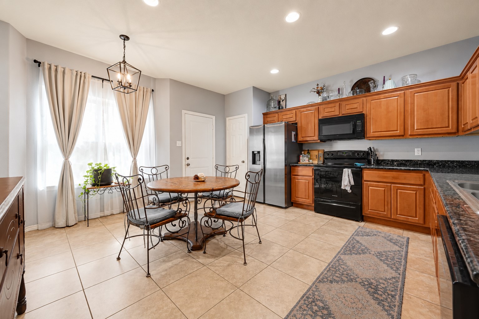 A spacious kitchen with warm wood cabinetry, granite countertops, and modern appliances, complemented by a cozy dining area with elegant lighting and natural light from large windows. A spacious kitchen with warm wood cabinetry, granite countertops, and modern appliances, complemented by a cozy dining area with elegant lighting and natural light from large windows.
