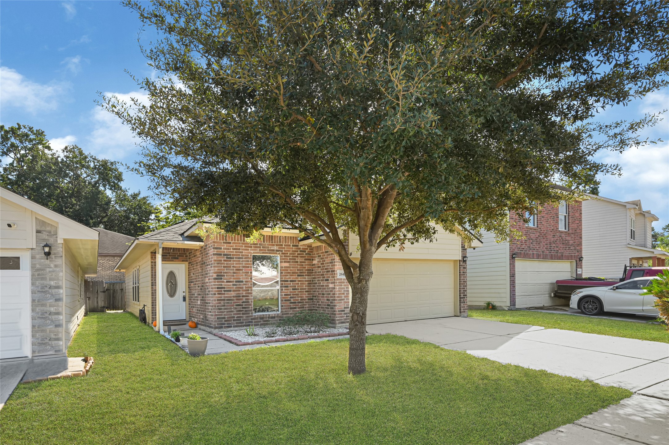 Charming brick home with a spacious front yard and mature tree, featuring a two-car garage and inviting entryway in a quiet neighborhood.