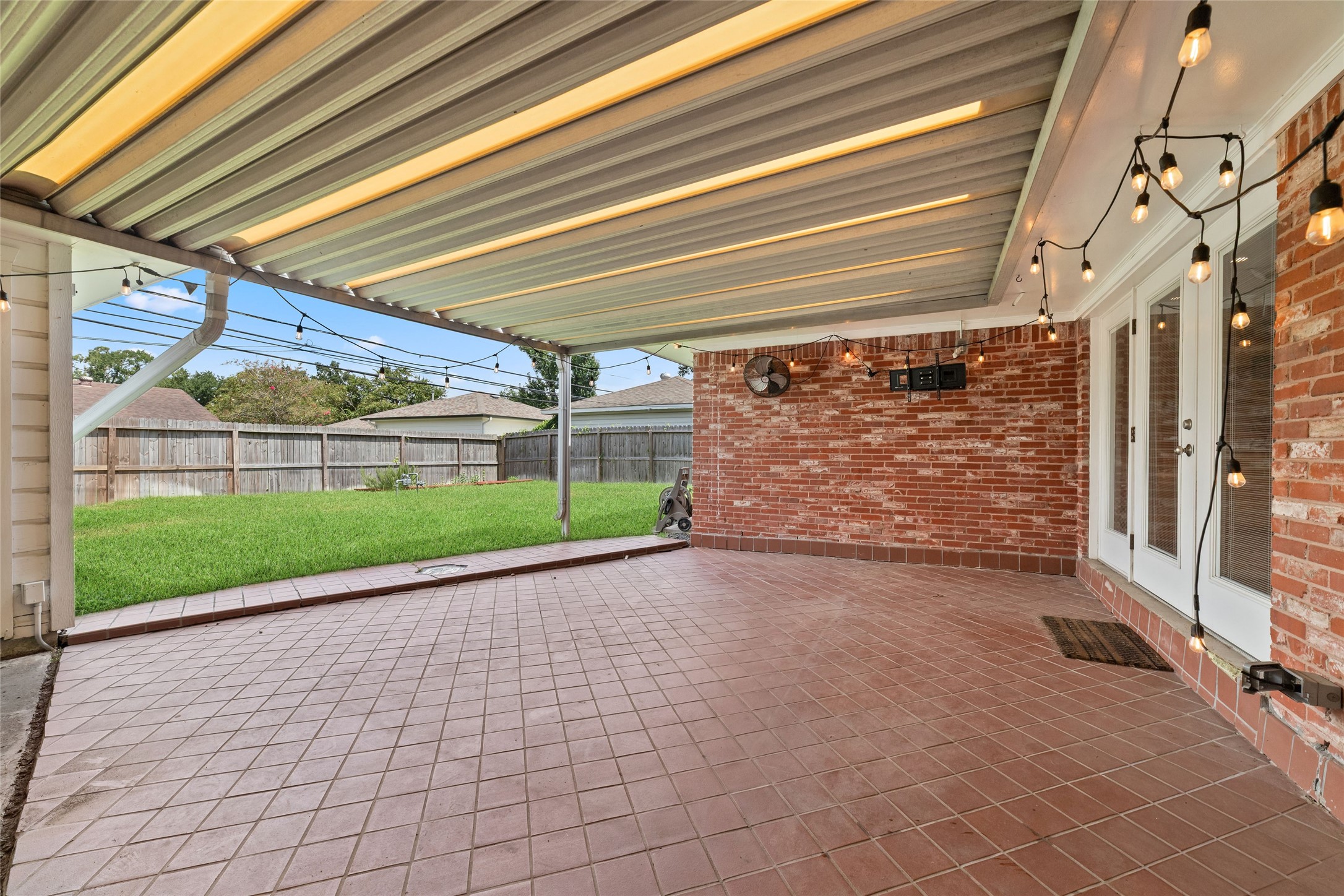 Spacious covered patio perfect for outdoor entertaining, overlooking a lush green yard complete with raised garden beds.
