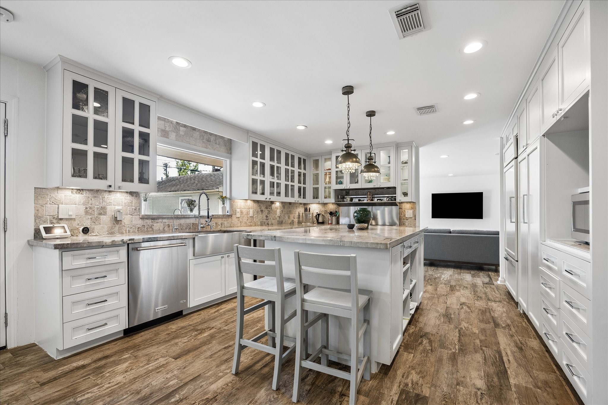 Beautifully updated kitchen features custom white cabinetry, glass-front upper cabinets, stone countertops, tile backsplash, stainless steel appliances & a large island w/breakfast bar seating. Decorative pendant lighting adds a distinctive touch.