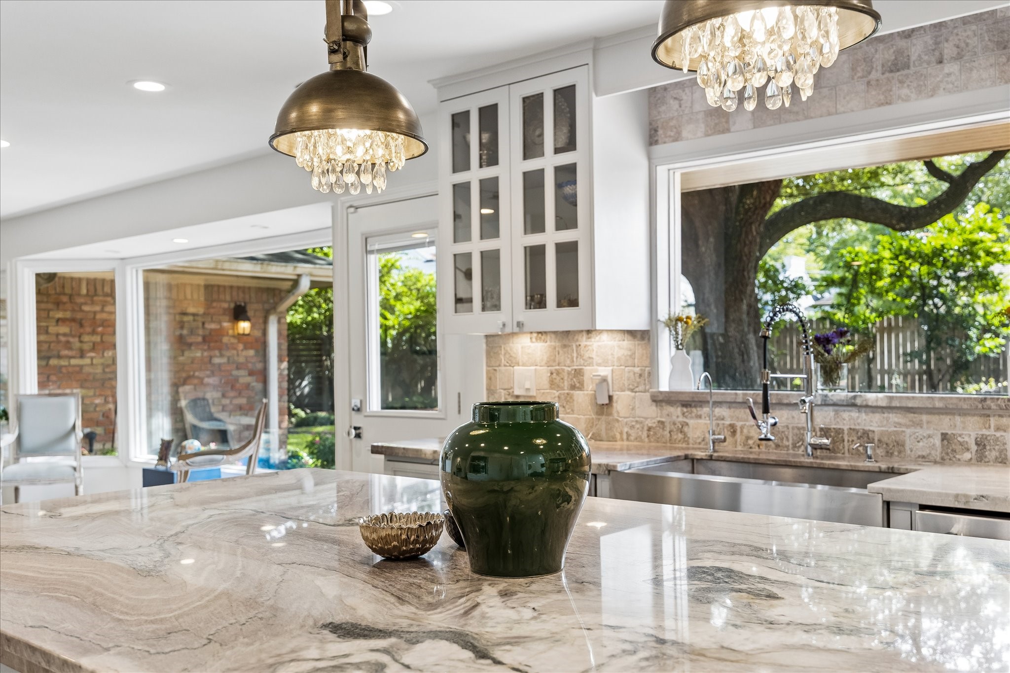 Closer look at the gorgeous stone countertops, decorative pendant lighting & farmhouse-style stainless steel sink w/statement faucet. Large windows bring in natural light & offer views of the backyard.