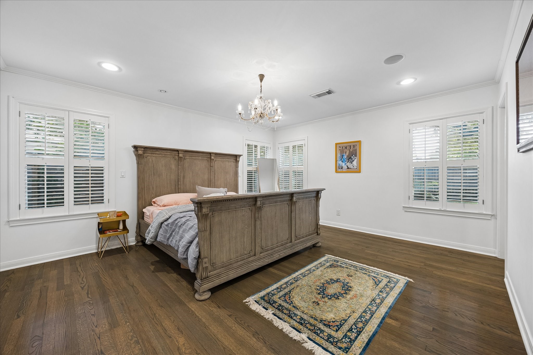 Spacious primary bedroom features beautiful hardwood floors, crown molding, recessed lighting & an elegant chandelier. Multiple windows w/plantation shutters fill the room w/natural light.