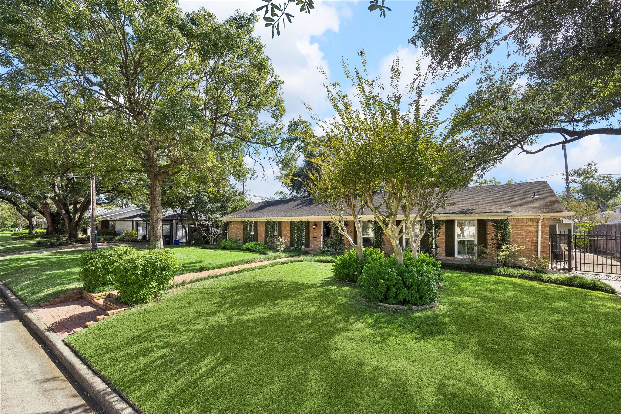 Beautiful one-story brick home in Afton Oaks, surrounded by mature trees & lush landscaping. Expansive front lawn, manicured hedges, & gated driveway add to the inviting exterior.