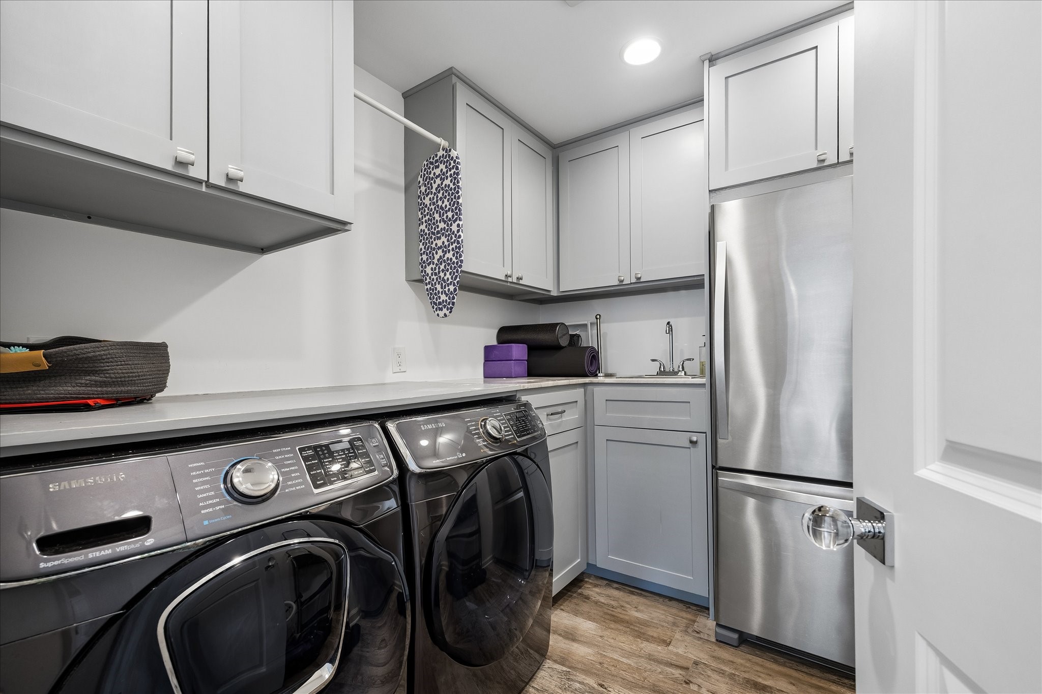 Well-appointed utility room features full-size washer & dryer, extensive upper & lower cabinetry, countertop workspace, utility sink & additional refrigerator. Recessed lighting & wood-look flooring complete this functional space, offering excellent storage & convenience for everyday household needs.