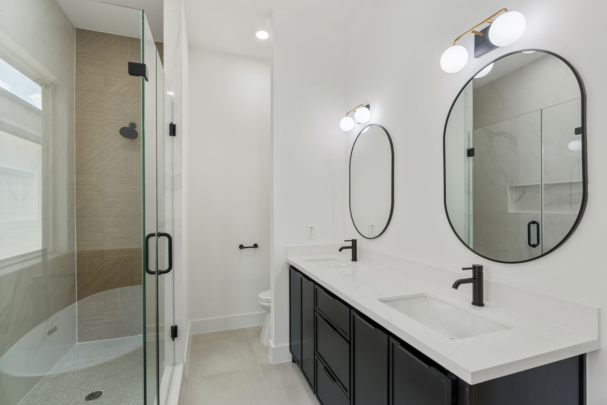 Elegant bathroom featuring a spacious glass enclosed shower, dual vanity with sleek black fixtures, and modern lighting.