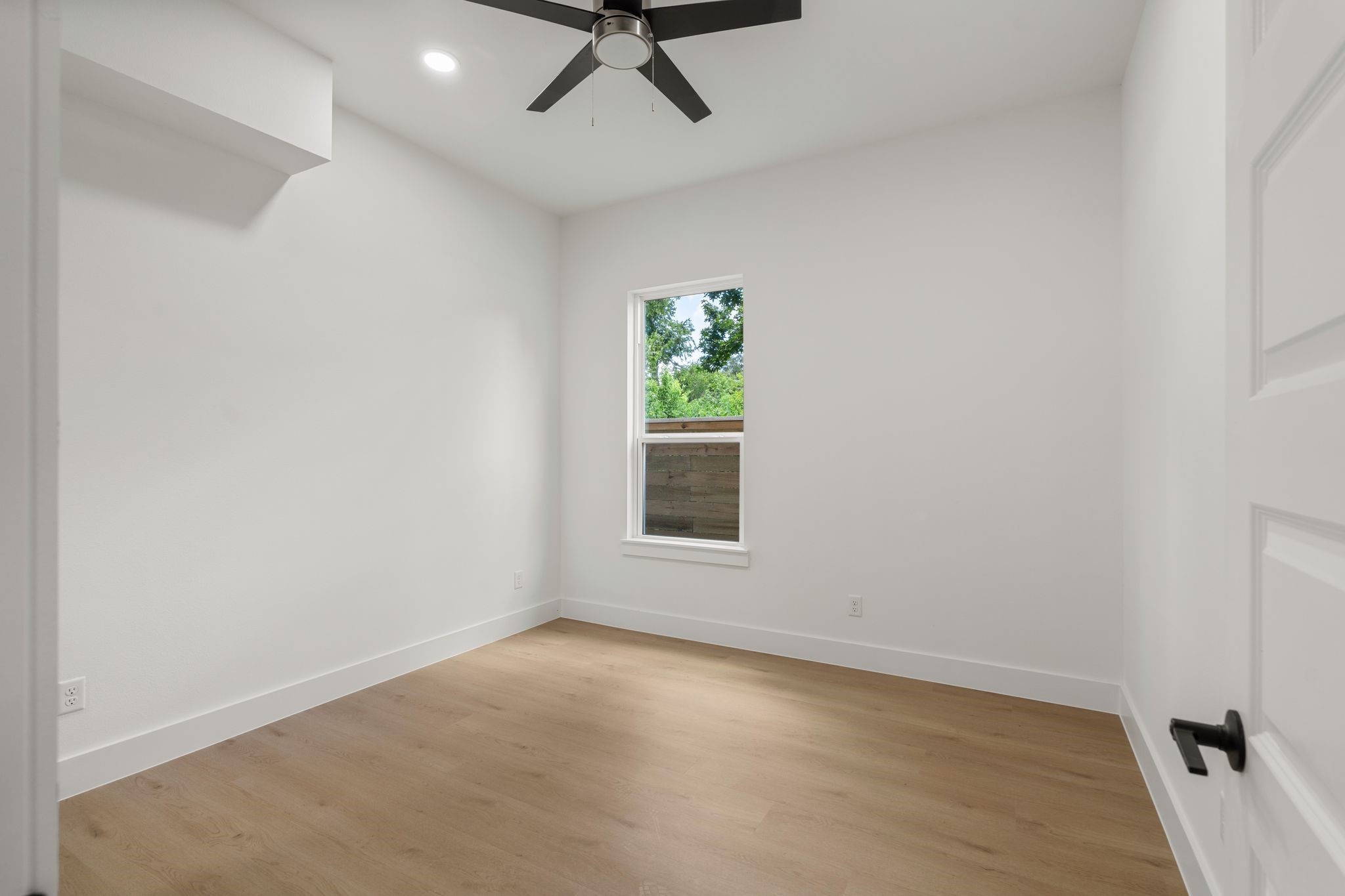 Bright and inviting room with sleek hardwood floors, crisp white walls, and a modern ceiling fan, perfect for a cozy retreat.