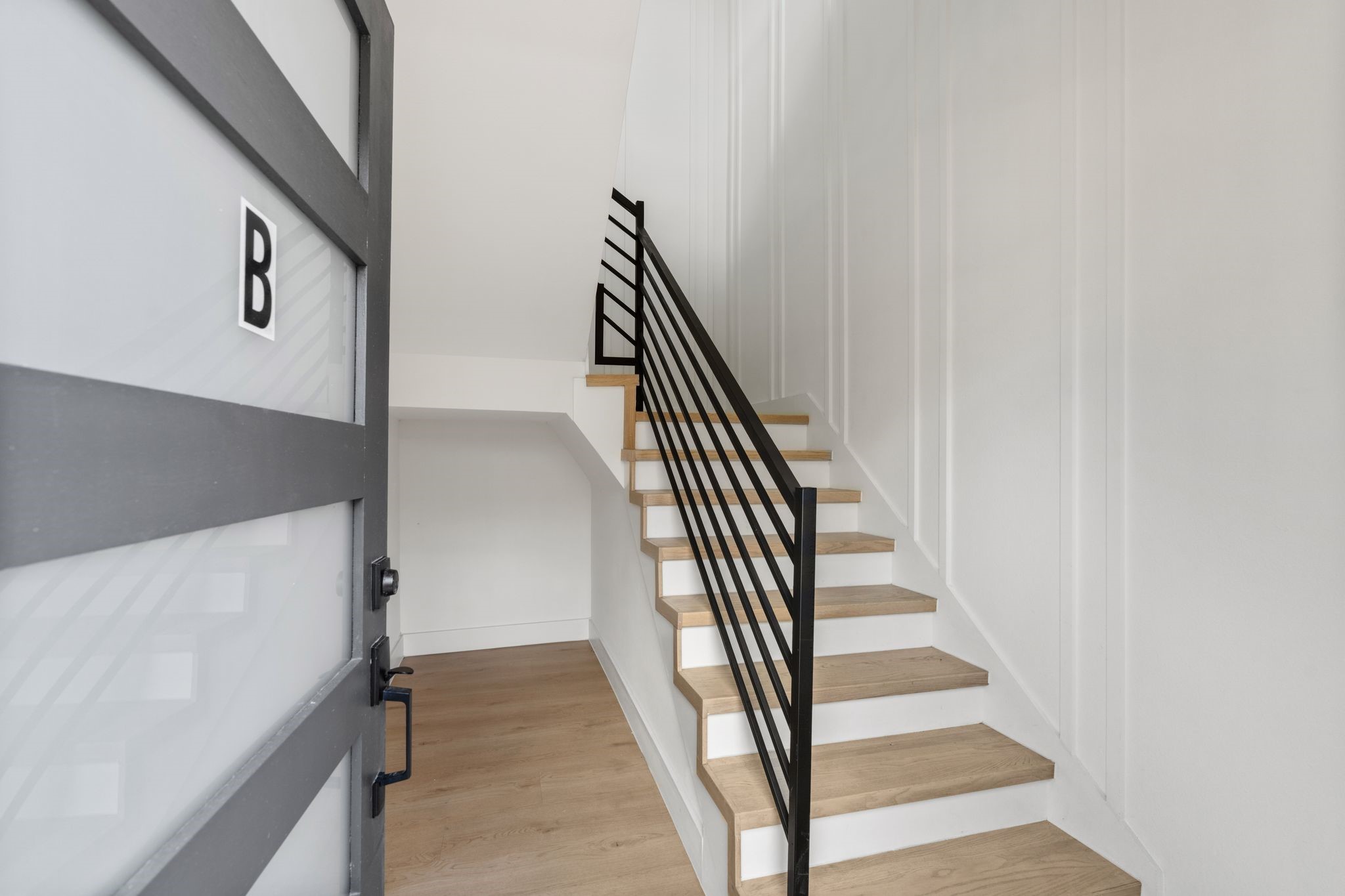 Contemporary entry way featuring sleek wooden stairs with modern black railings and minimalist white walls, creating a clean and inviting first impression.