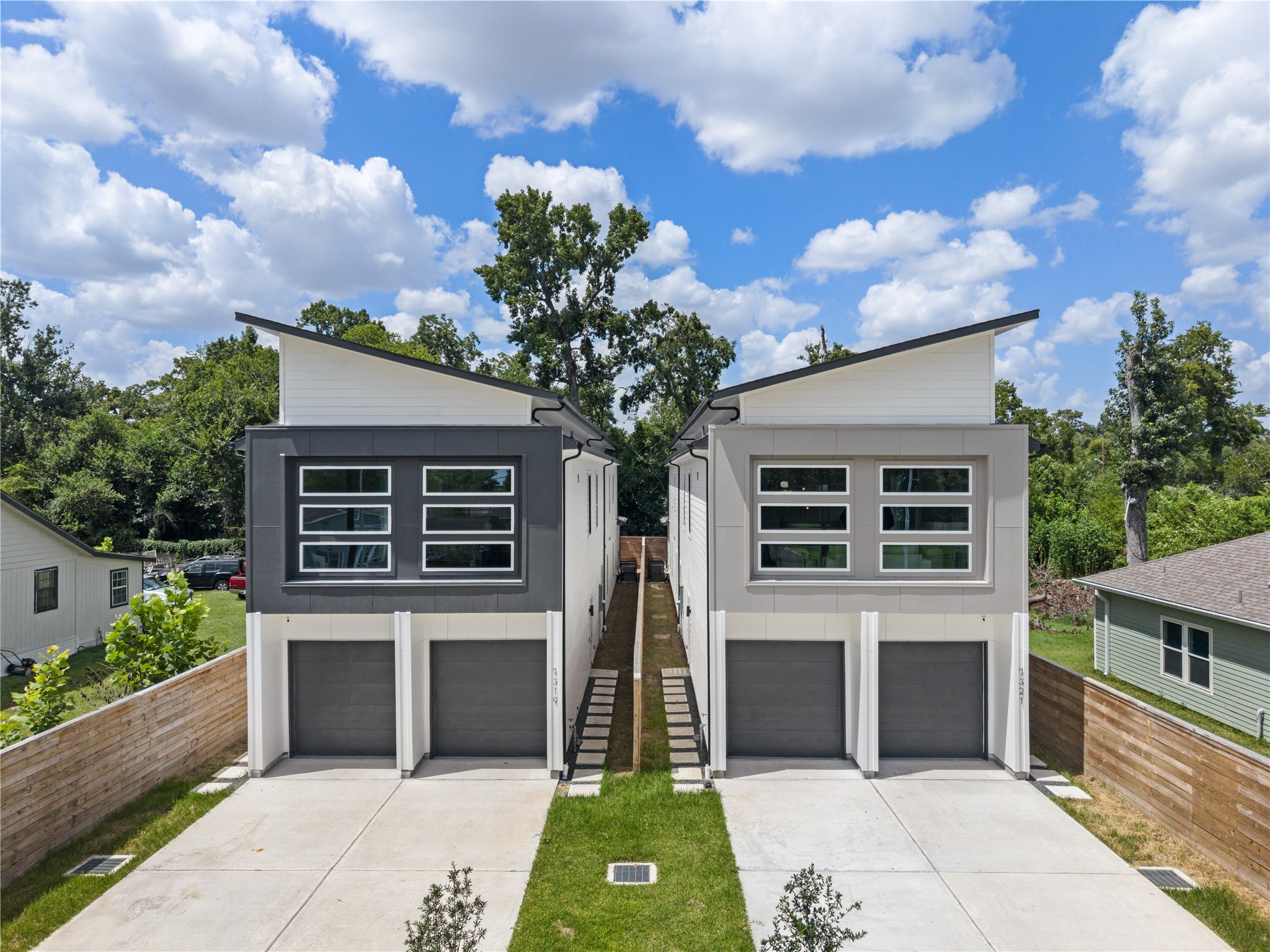 Modern duplex featuring sleek, angular rooflines and large windows for ample natural light. Eachunit offers a private garage and a shared driveway, surrounded by a lush, tree-lined setting