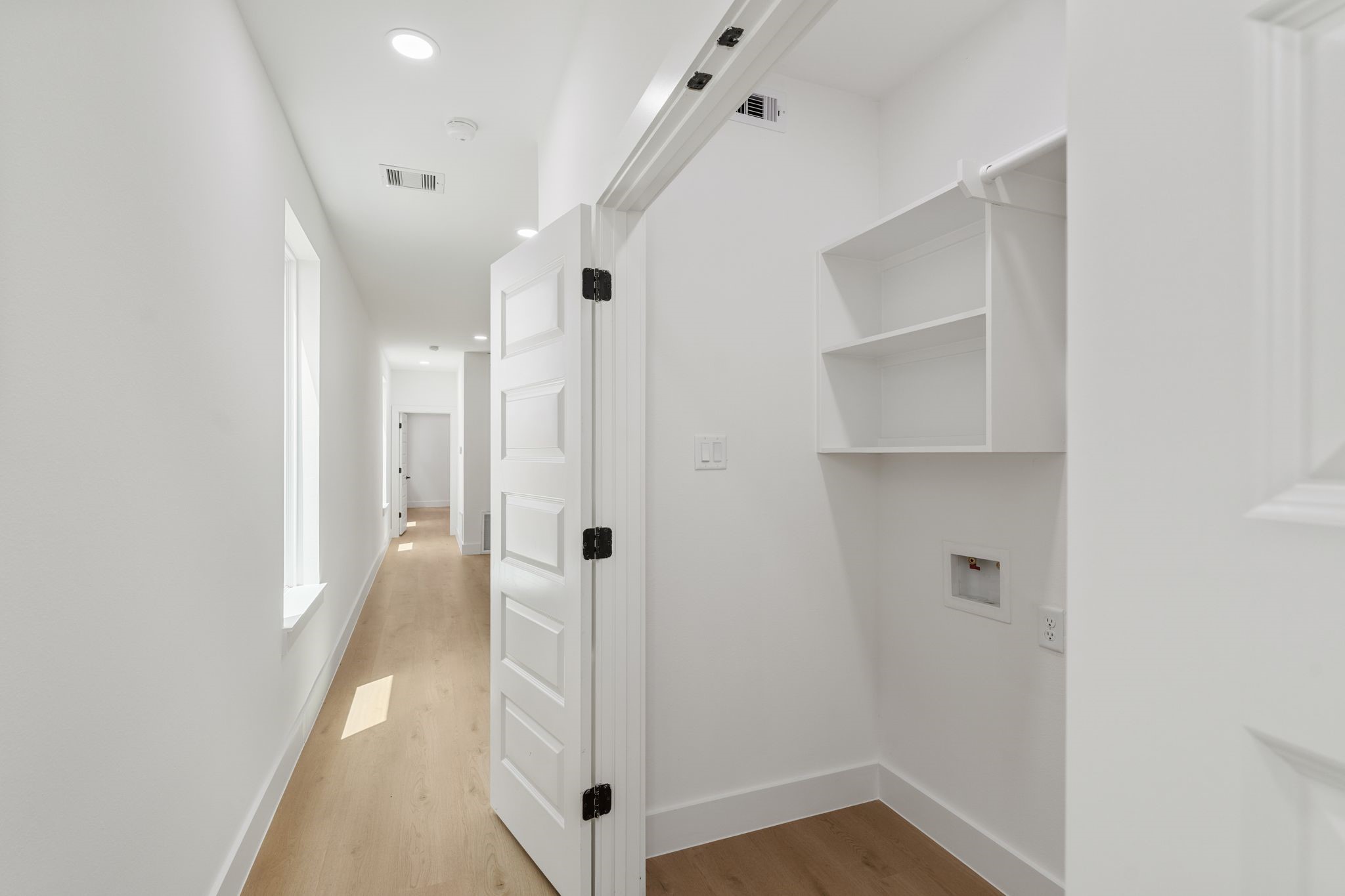Bright and inviting hallway with sleek wooden flooring leads to a utility room featuring built-in shelving and modern fixtures.