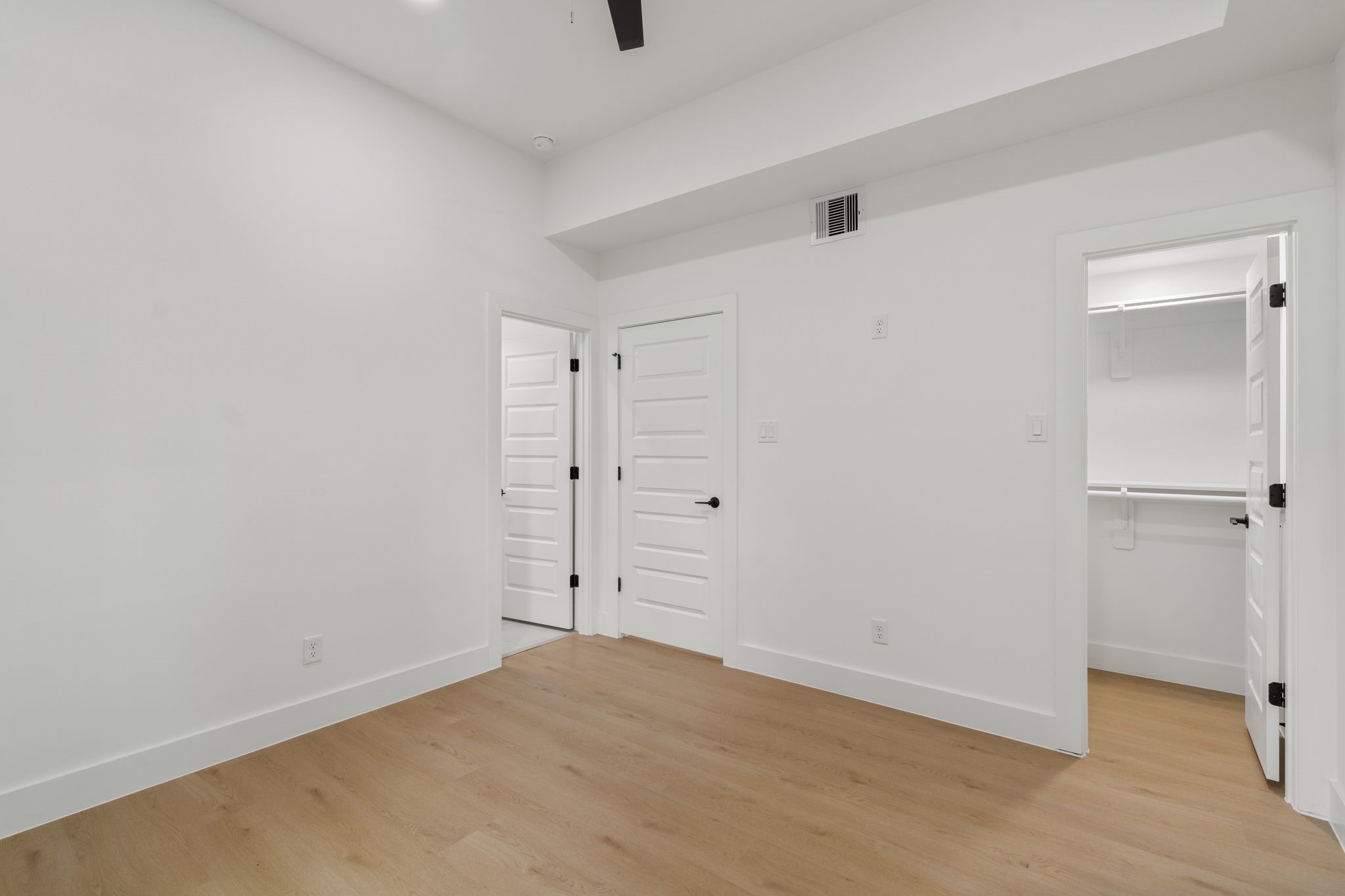 Bright and spacious room with sleek hardwood floors, white walls, and modern doors leading to ample closet space.