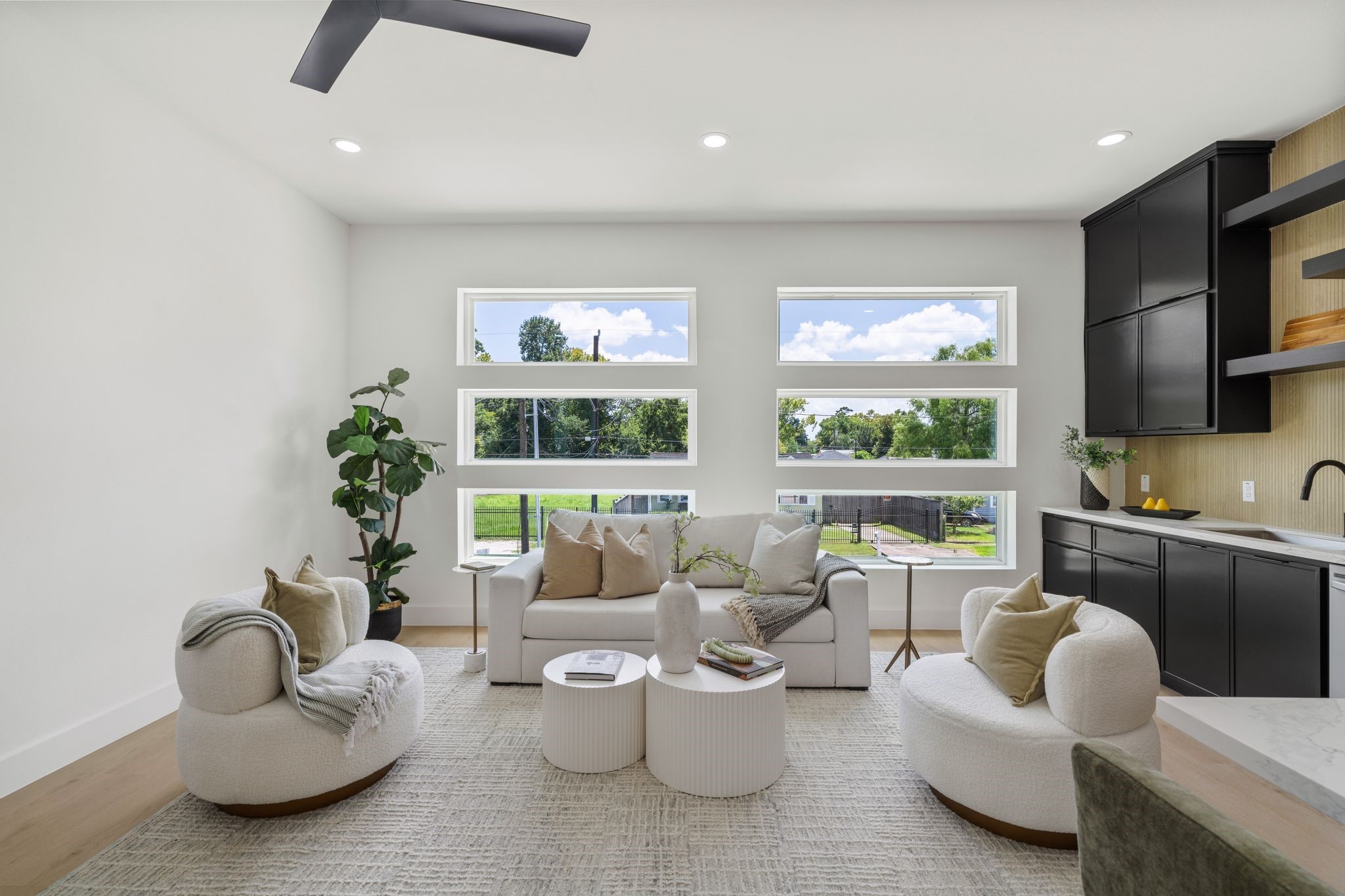 Bright and modern living space with large windows, cozy seating, and sleek black cabinetry, offering a perfect blend of comfort and style.