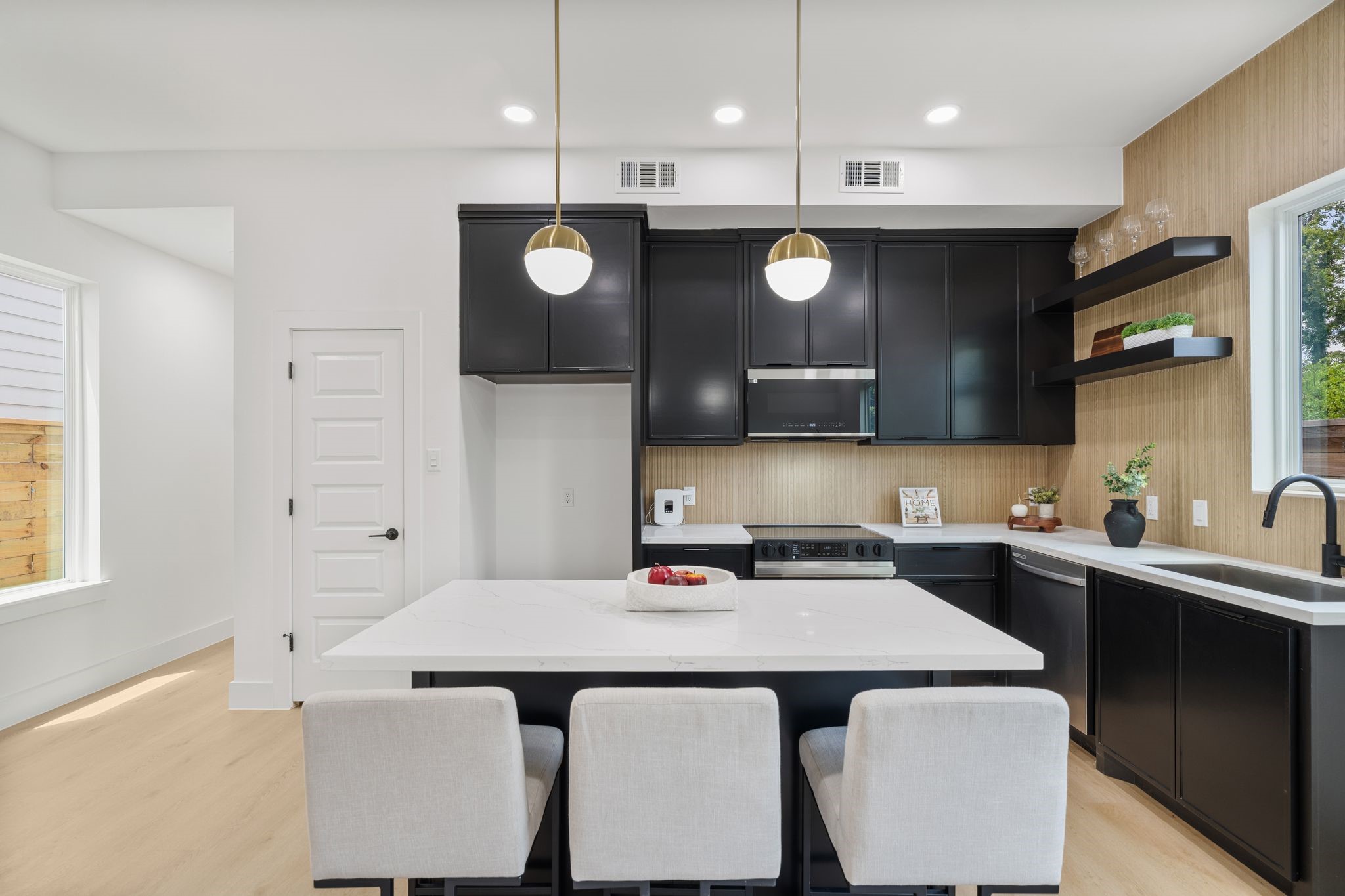 Sleek modern kitchen featuring black cabinetry, elegant gold pendant lighting, and a spacious white island with seating.