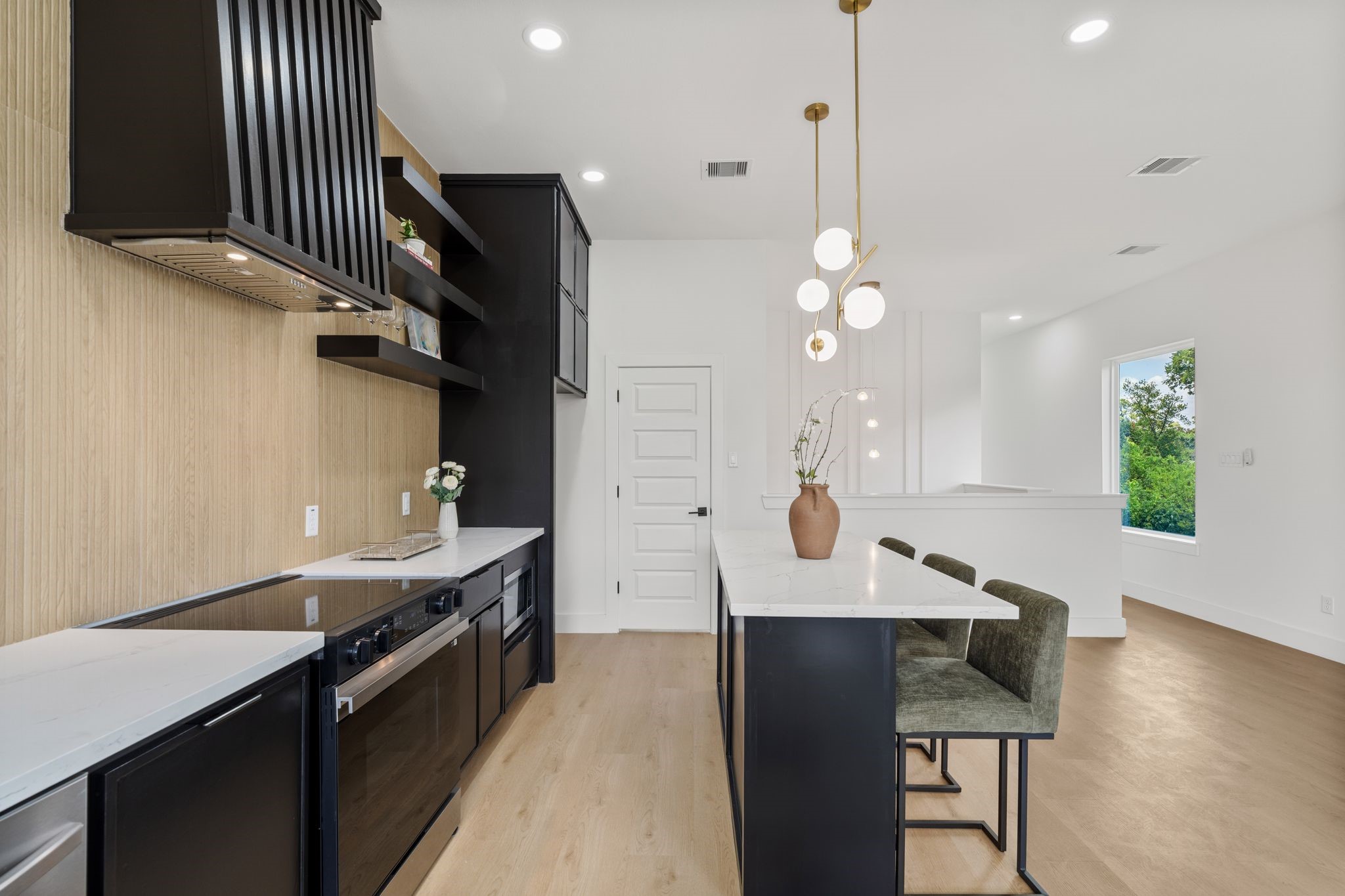 Sleek modern kitchen with black cabinetry, elegant pendant lighting, and a spacious island with seating, all set against warm wood flooring and a bright, open layout.