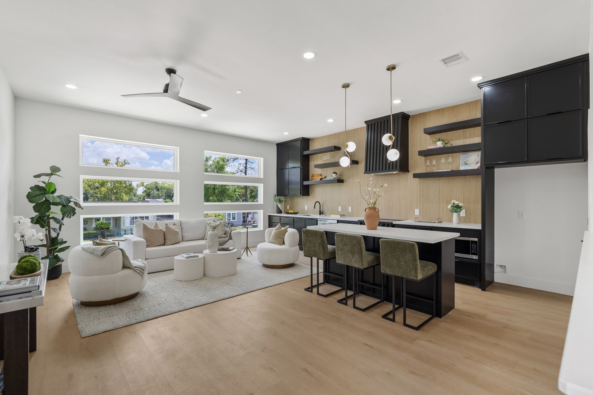 Spacious open-concept living area with modern kitchen, featuring sleek black cabinetry, stylish pendant lighting, and large windows that flood the space with natural light