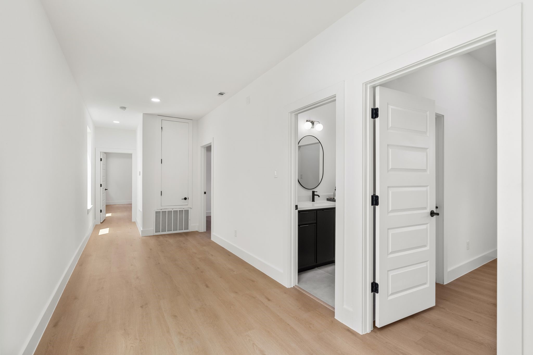 Bright and spacious hallway with sleek wood flooring and modern finishes, leading to multiple rooms and a stylish bathroom.