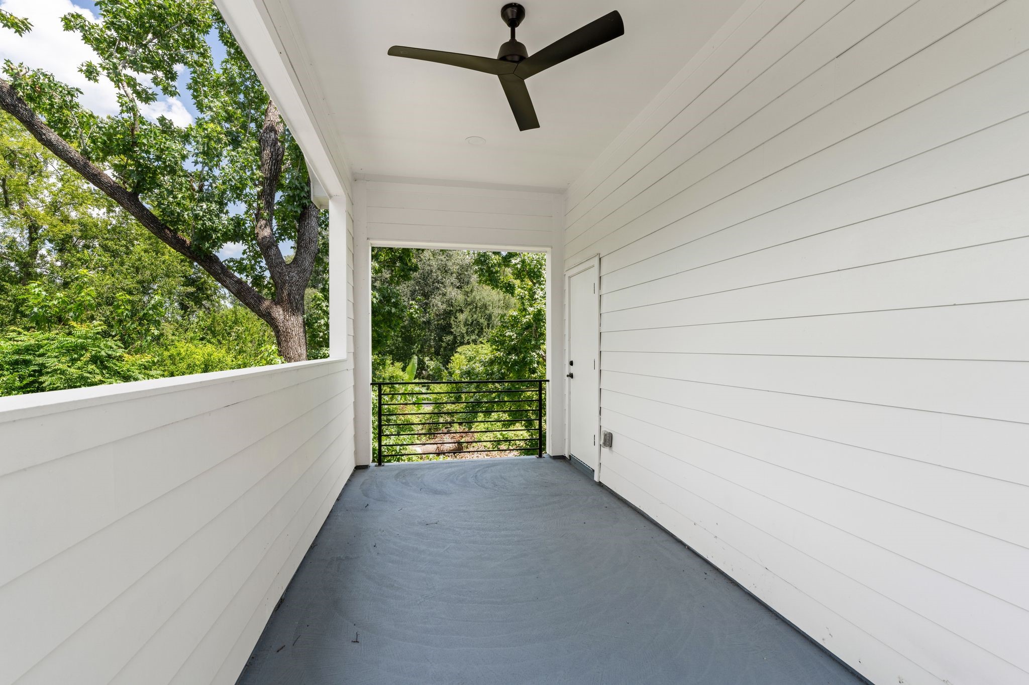 Spacious covered balcony with a ceiling fan, offering serene views of lush greenery.