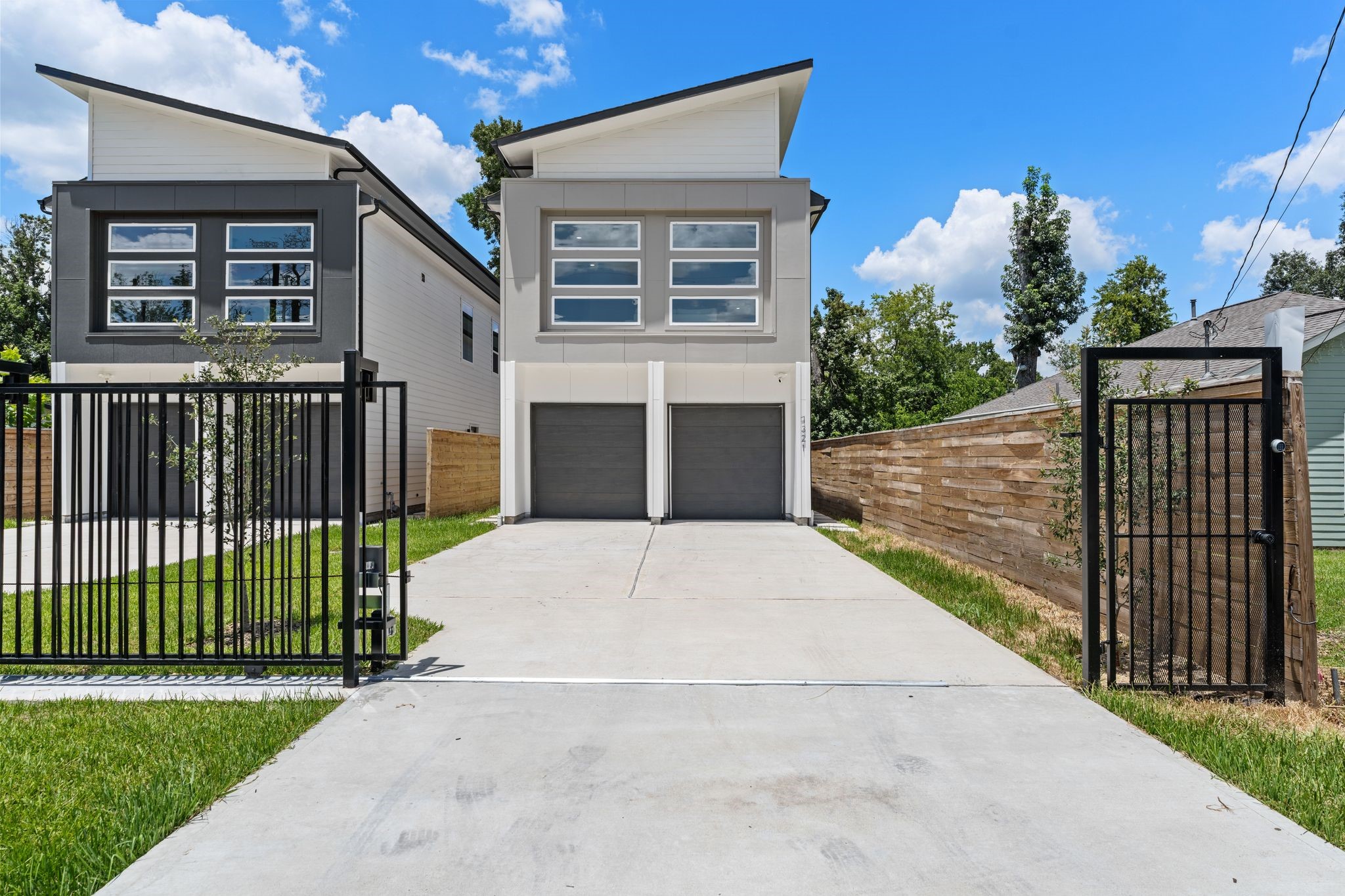 Modern new construction luxury duplexes with sleek lines and large windows are set behind a secure black iron gate, featuring a long shared driveway and well and private garages. Modern new construction luxury duplexes with sleek lines and large windows are set behind a secure black iron gate, featuring a long shared driveway and well and private garages.