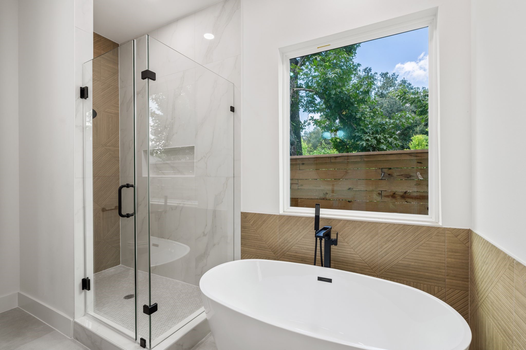 Elegant bathroom featuring a spacious glass enclosed shower, modern dual sinks, and a luxurious free standing bathtub with a serene view.