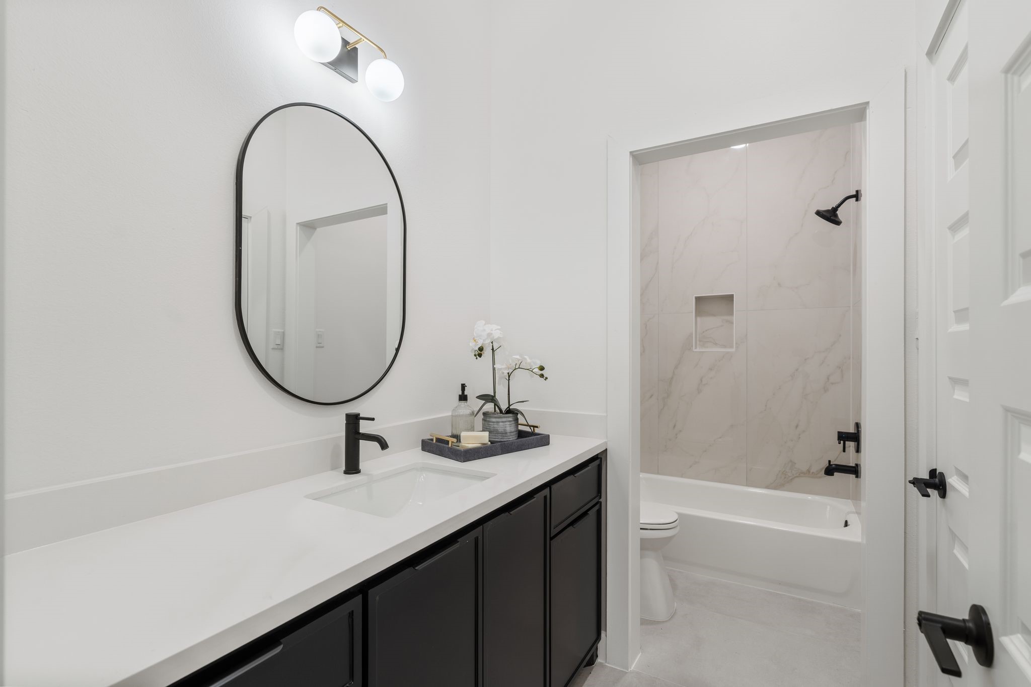 Sleek modern bathroom featuring a chic black vanity with dual sinks, an elegant oval mirror, and a bathtub with stylish marble-look tile