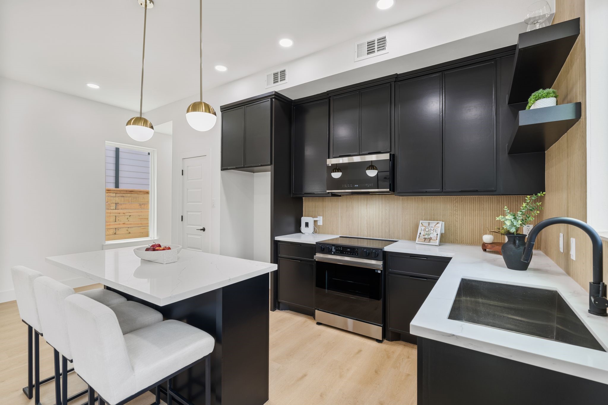 Sleek modern kitchen featuring black cabinetry, stainless steel appliances, and a spacious quartz island with seating. Elegant pendant lighting adds a touch of sophistication.