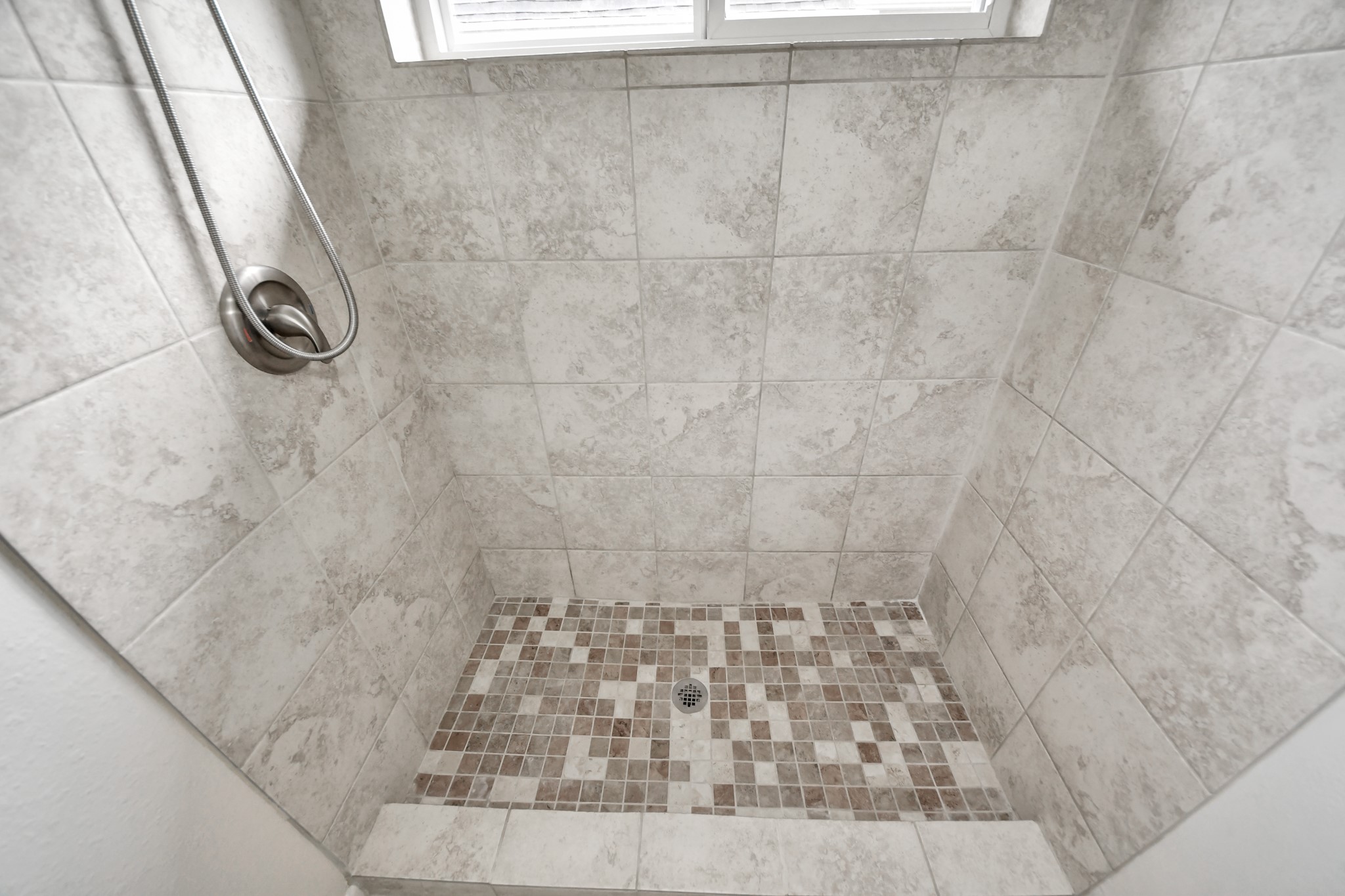Detailed view of the tiled walk-in shower with decorative mosaic tile floor.