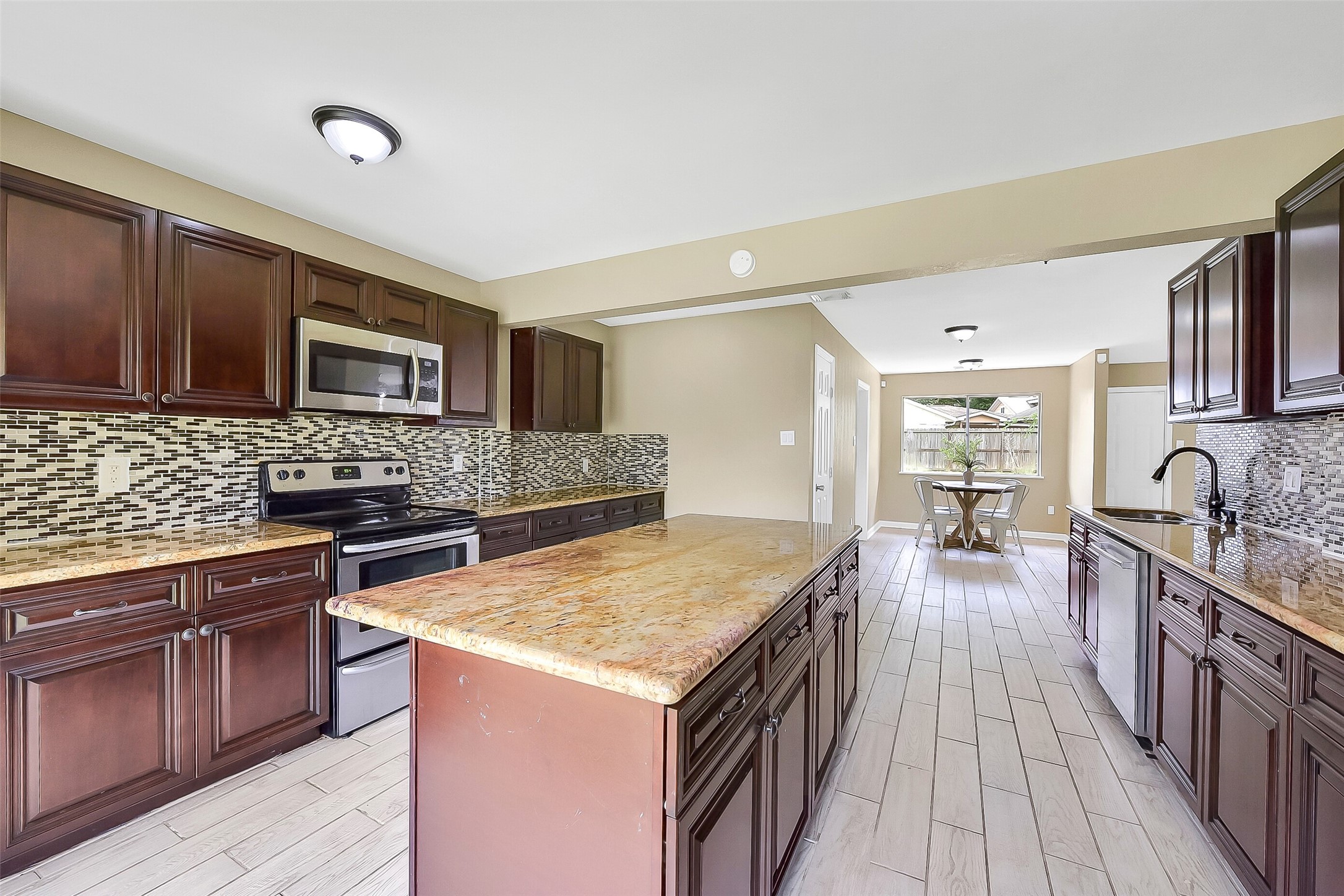 This updated kitchen features rich wood cabinetry, exotic granite countertops, a stylish mosaic glass tile backsplash, stainless appliances, and a large center island with extra storage and workspace.