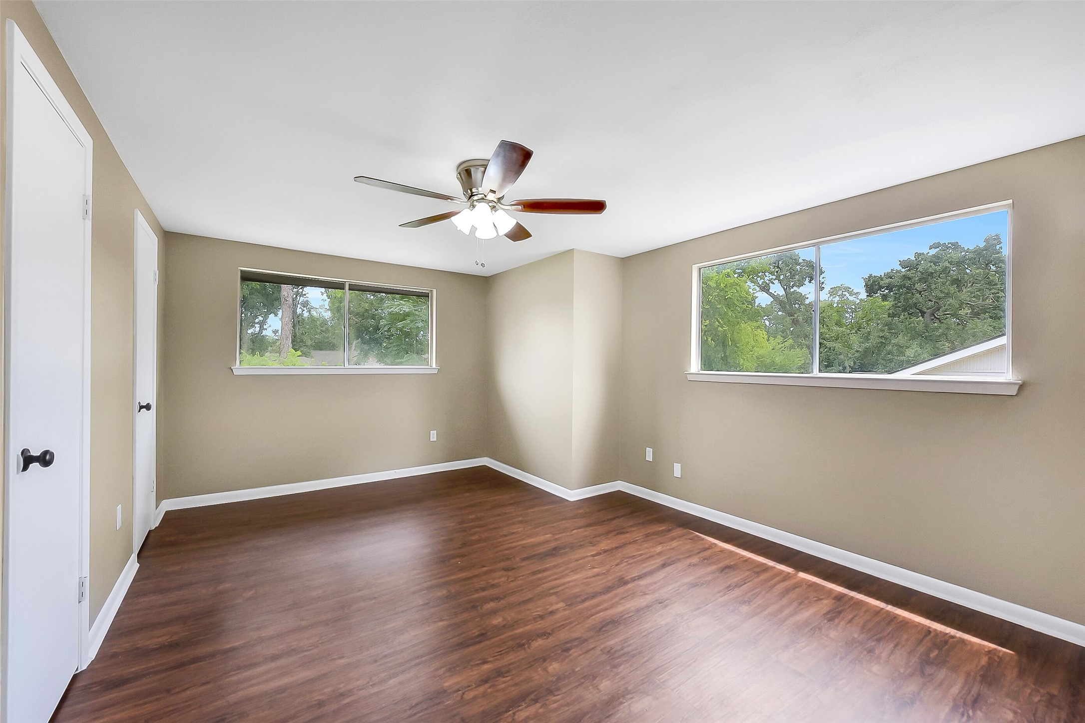 This upstairs bedroom features large windows for abundant natural light, wood-look flooring, dual closets, and a ceiling fan, creating a bright and versatile space.