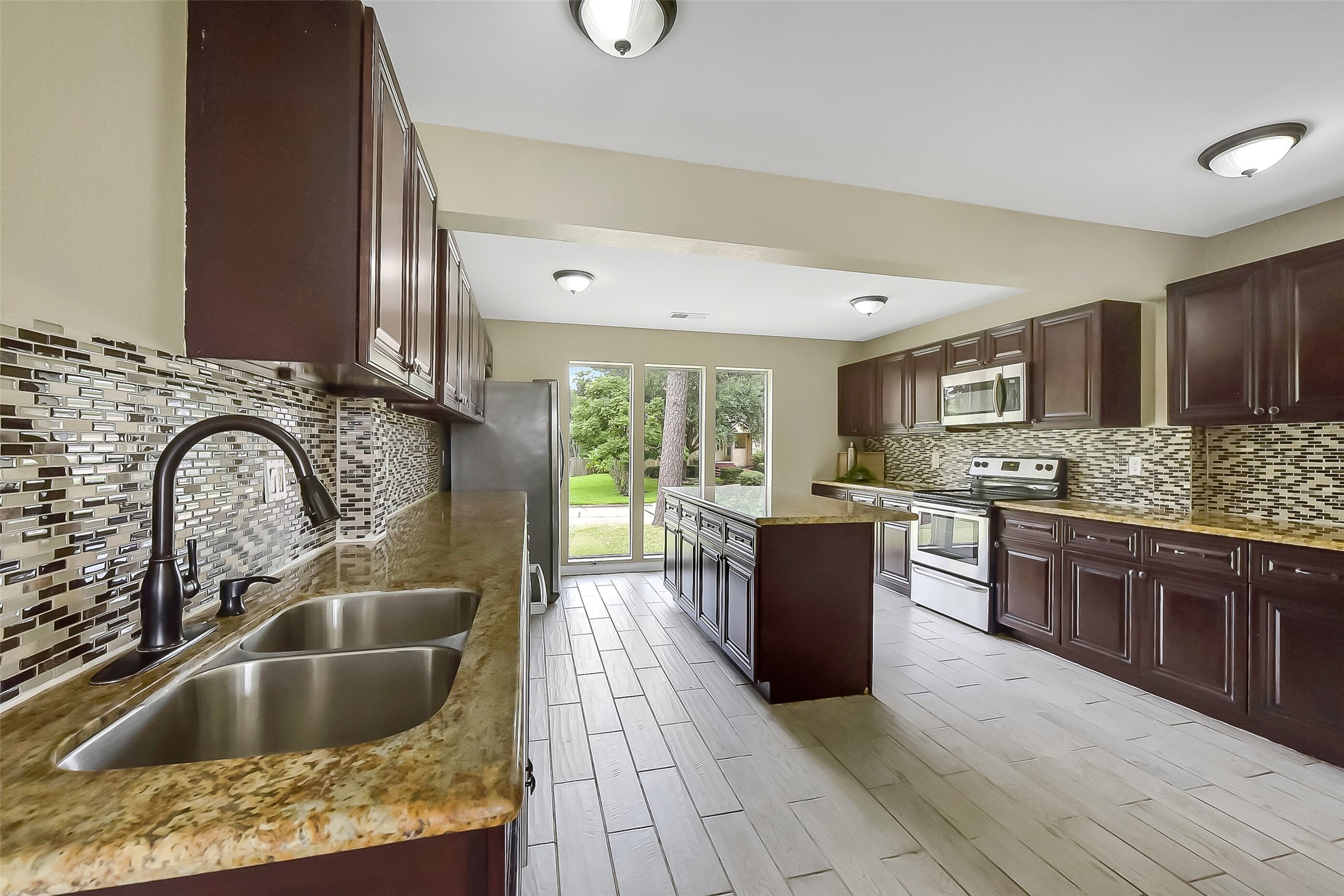 This kitchen is designed with the cook in mind, offering a full suite of stainless steel appliances including a built-in microwave, smooth glass top electric range, oven, and dishwasher. Rich wood cabinetry provides abundant storage, while granite countertops and a large center island create ample prep space.