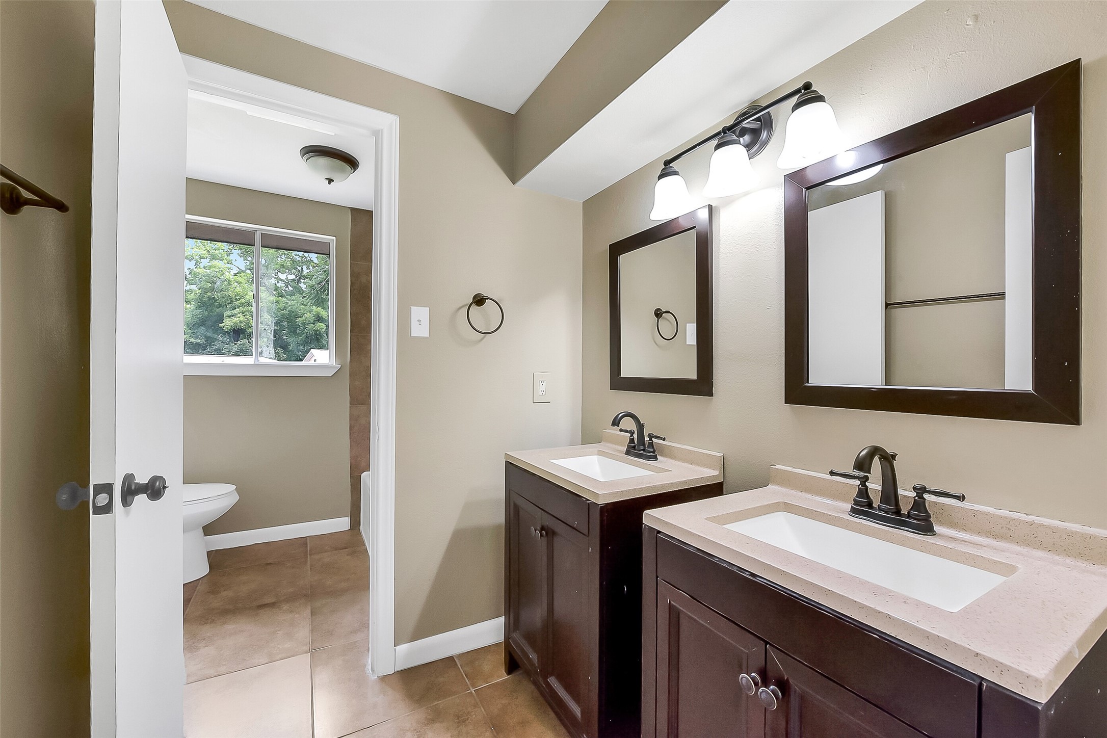 Upstairs full bathroom offers dual vanities with framed mirrors, updated fixtures, and a separate area with the tub/shower with a tile surround and toilet for added convenience.