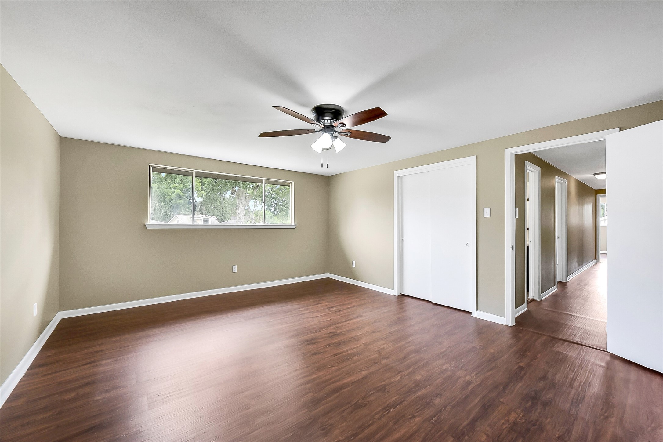 The fifth and final bedroom is generously sized and features wood-look flooring, a ceiling fan, and a large window that fills the space with natural light.